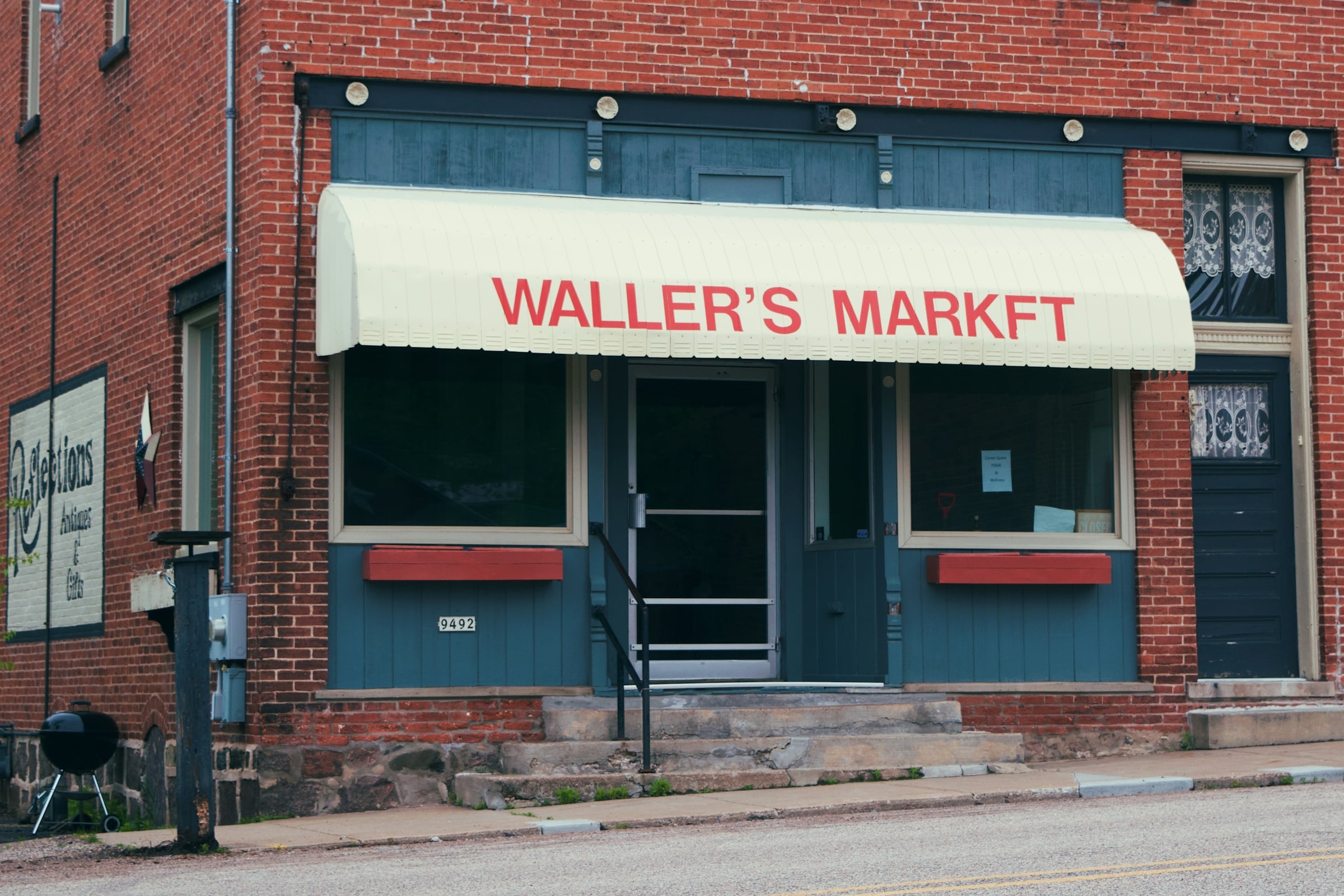 A small brick corner store with a cream fabric awning above plate-glass windows, fronting directly onto the sidewalk.