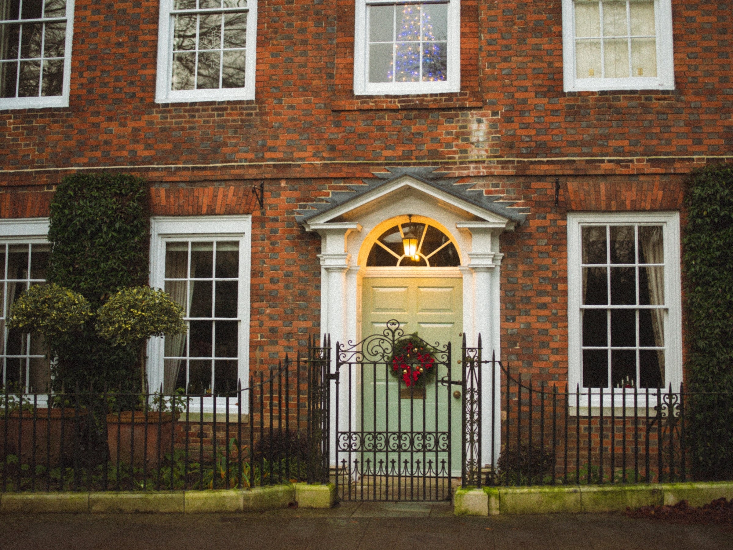 A red brick facade with a fanlight above a white panelled door and a wreath hanging on it