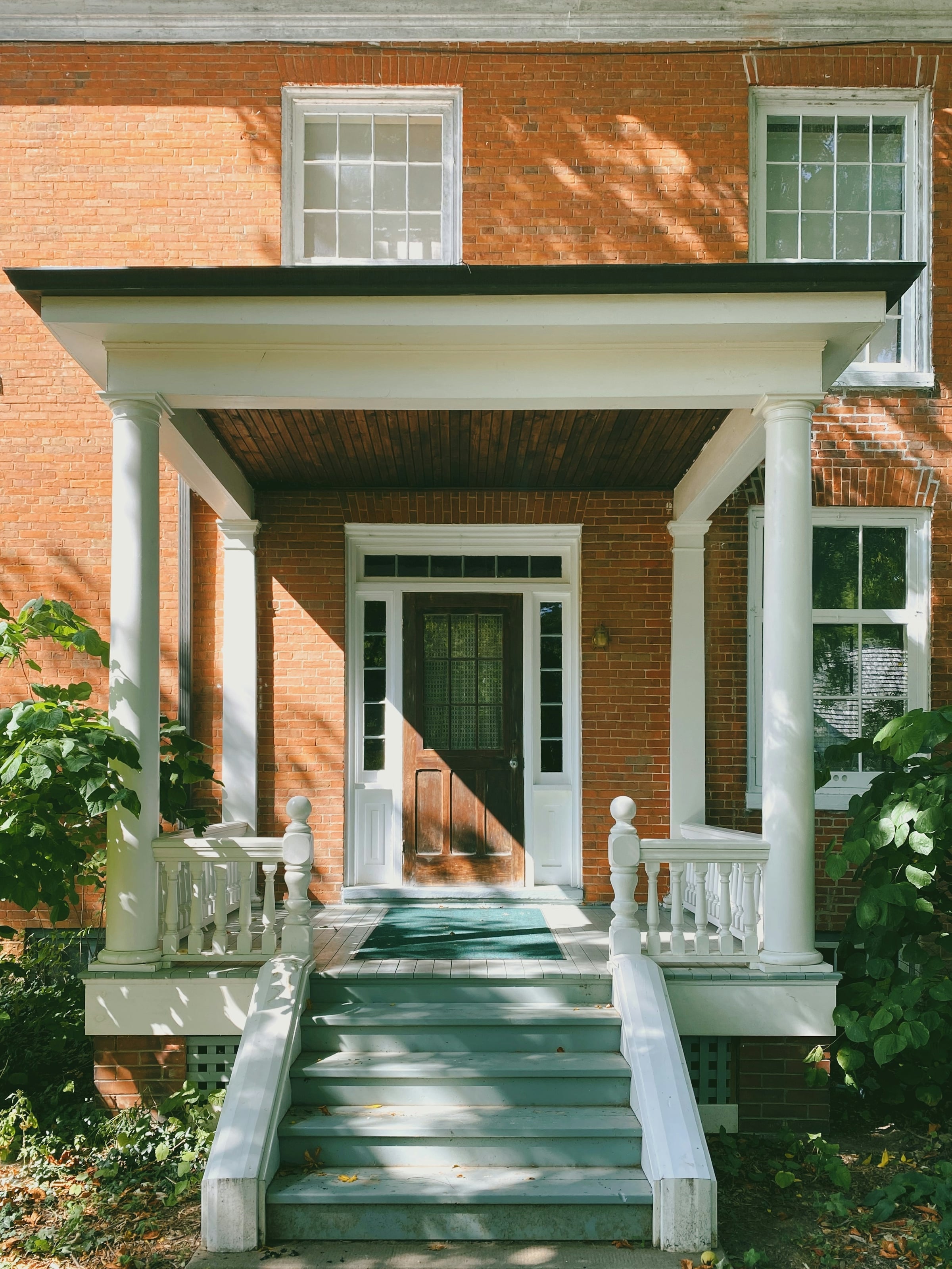 A brick house with a white columned front porch, balustrade and painted steps.