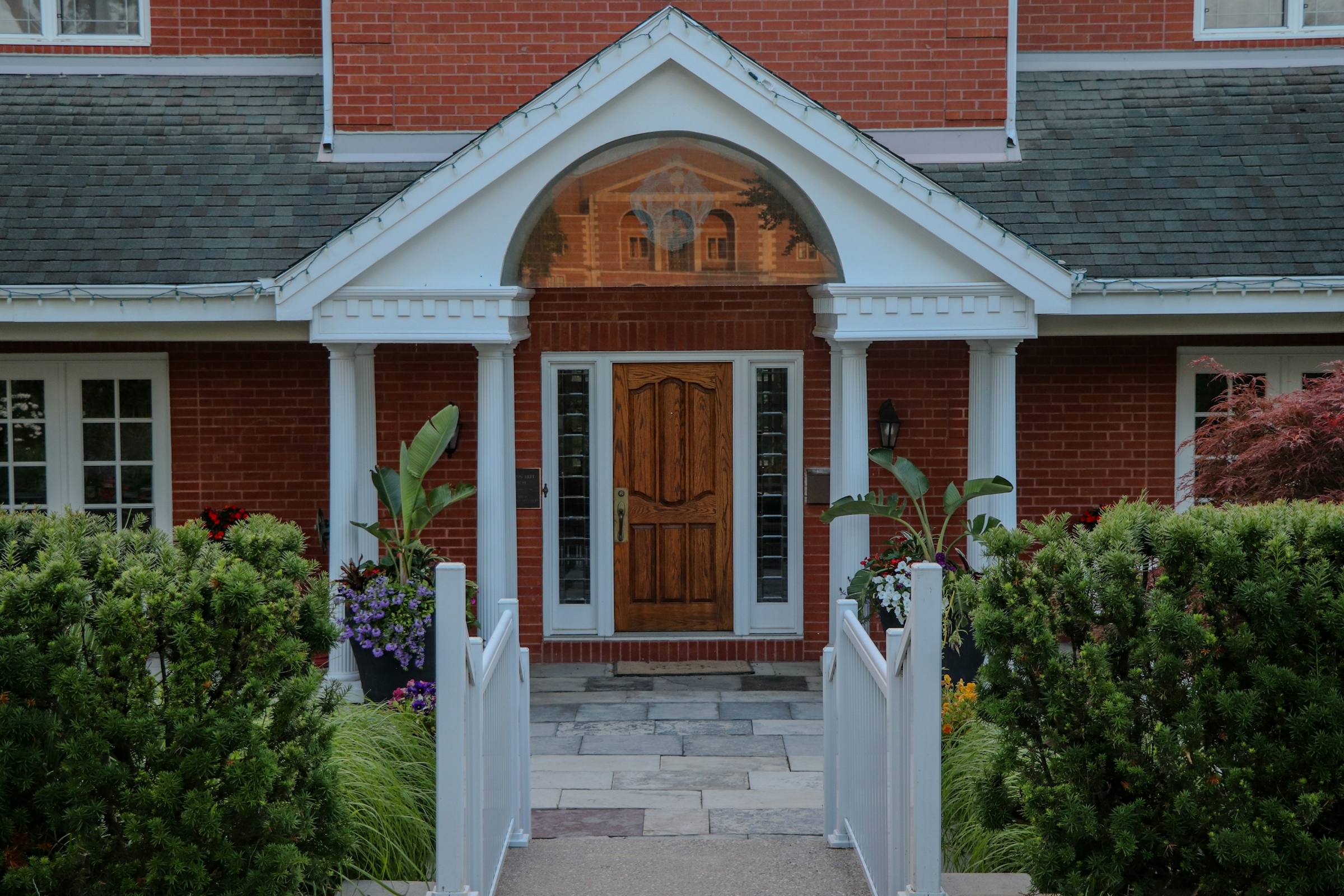 A red brick house with a white columned entrance portico framed by autumn foliage