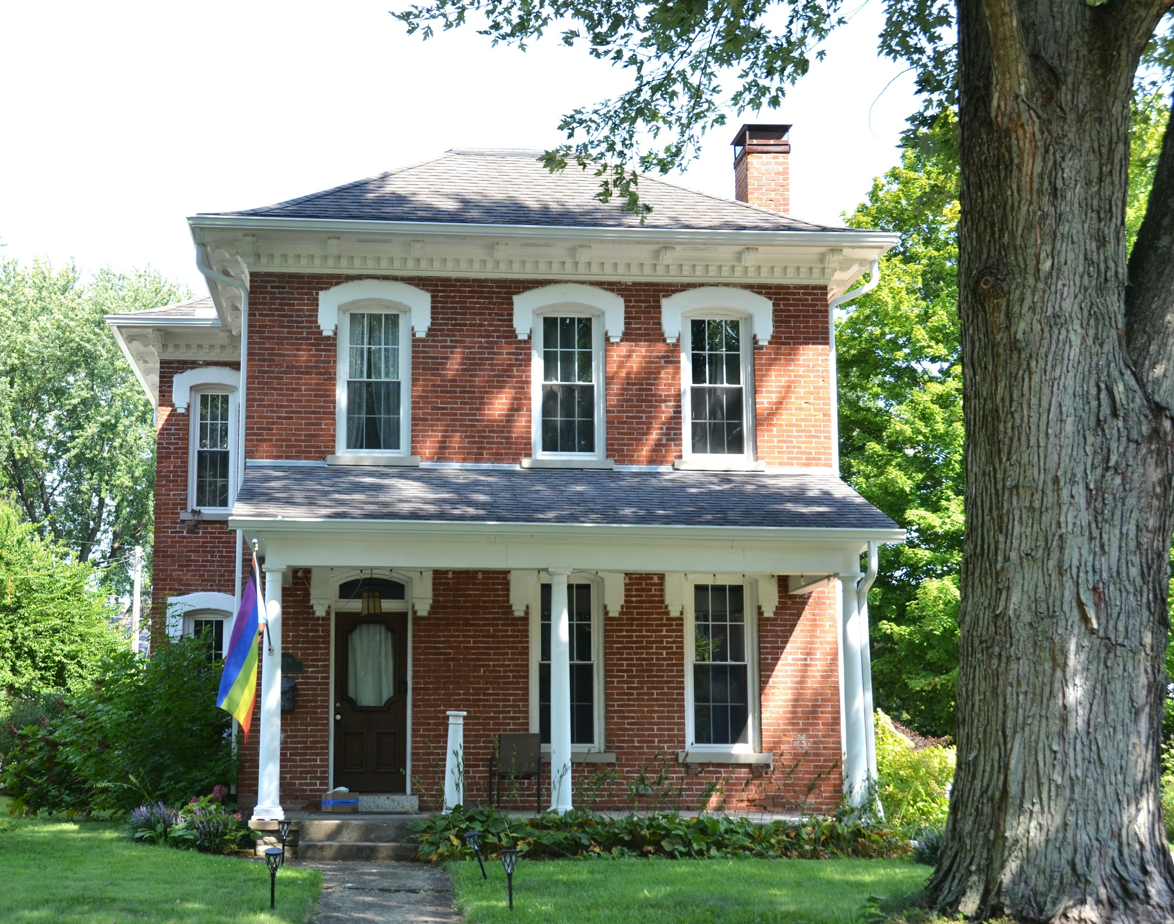A two storey red brick house with white trim and a flag hanging beside the upper windows
