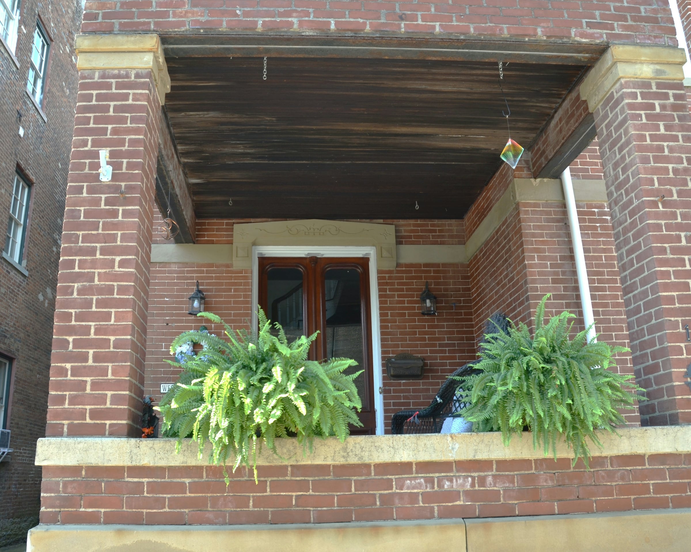 A brick porch with ferns hanging in baskets and potted plants beside the steps