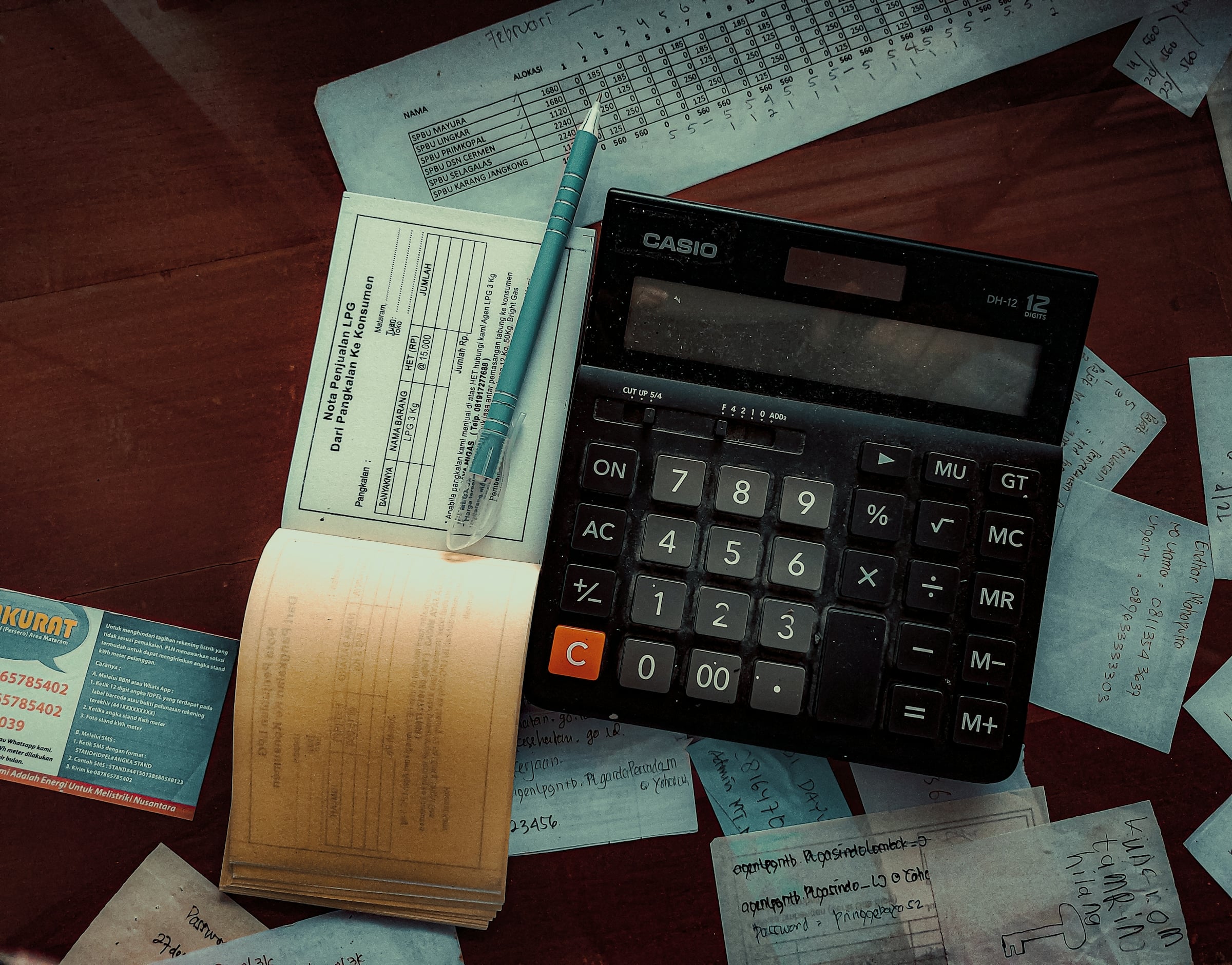 Desk calculator beside an open checkbook and scattered receipts on a wooden table