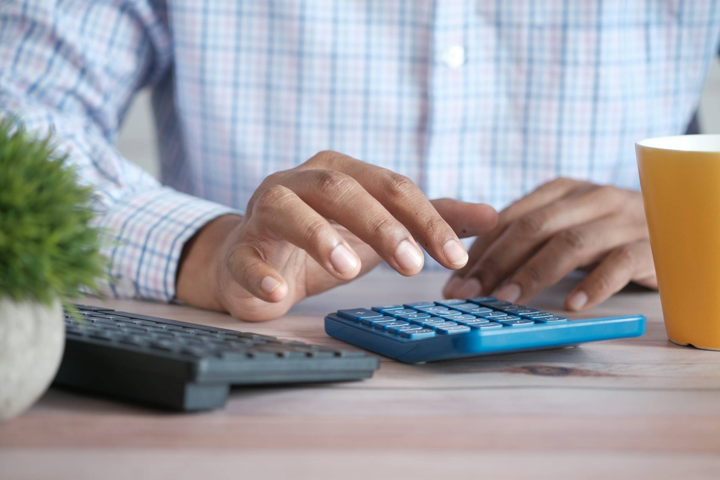 Hands working a desktop calculator beside a keyboard and a coffee cup