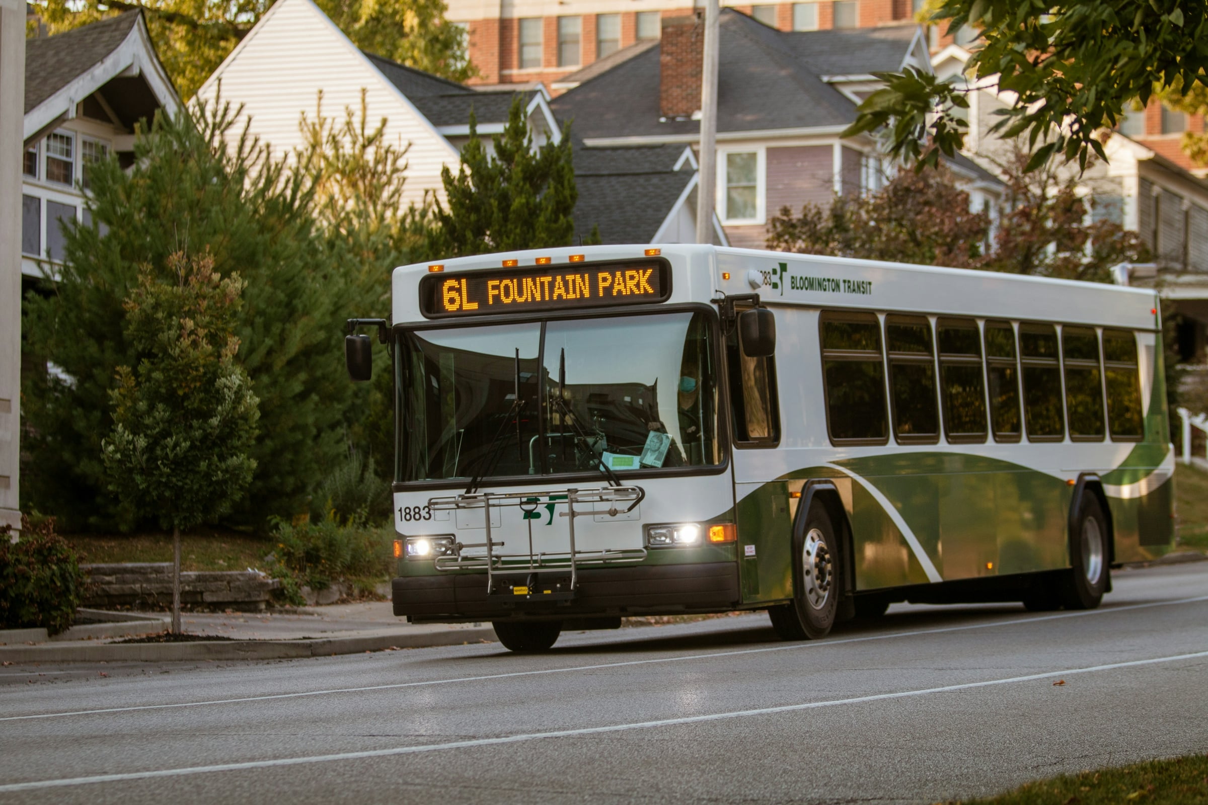 City transit bus driving along a tree-lined residential street past two-story houses
