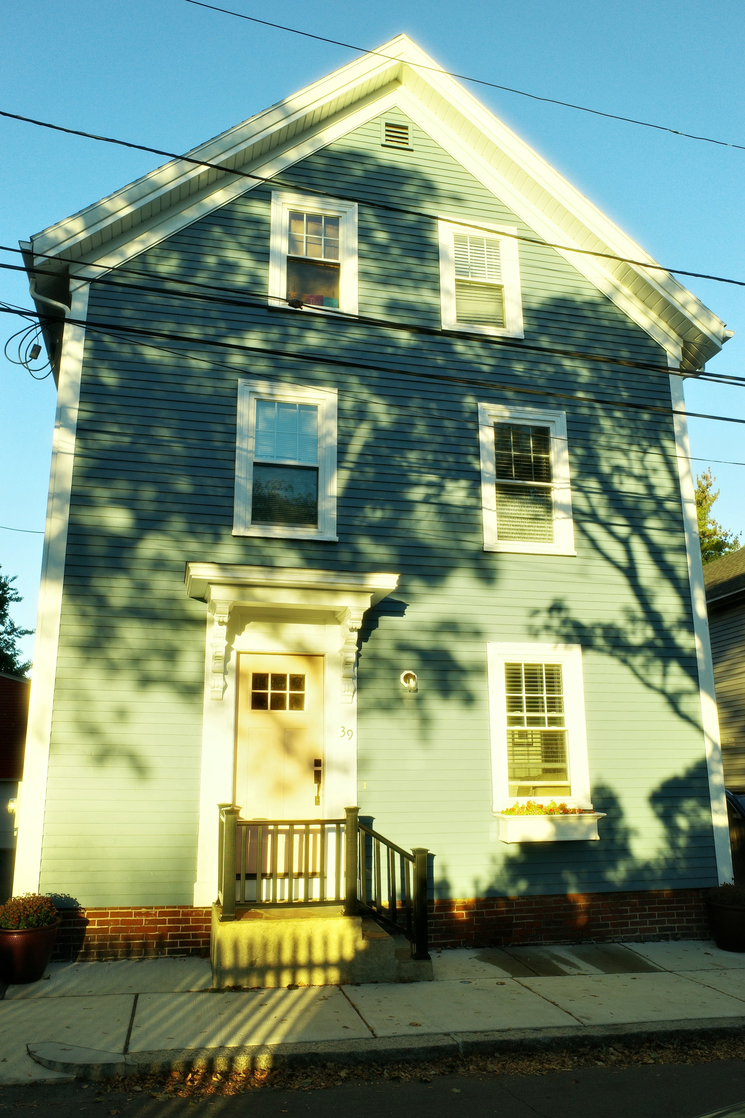 Pale green clapboard colonial house with a front porch in dappled sunlight