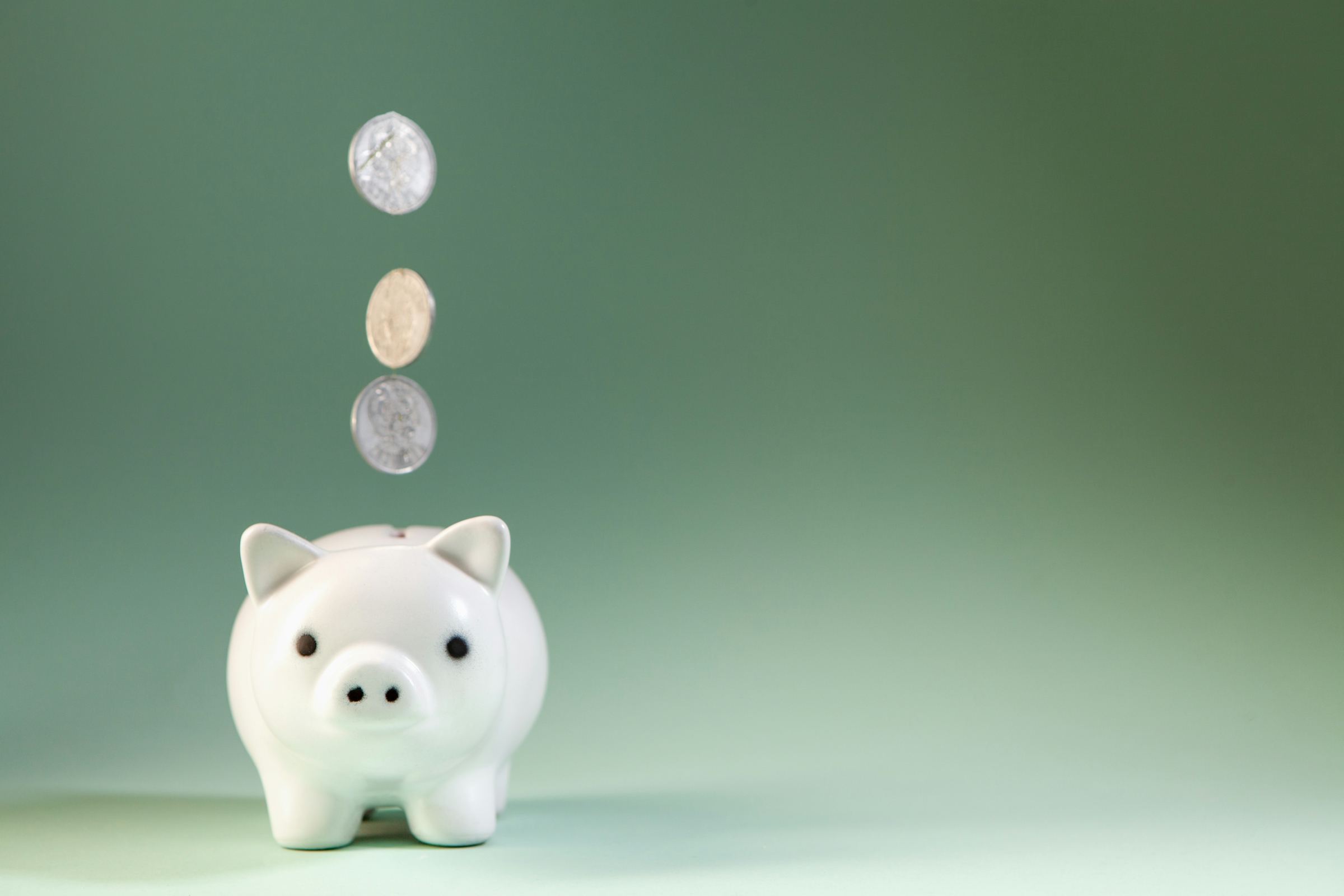 Coins dropping into a white ceramic piggy bank