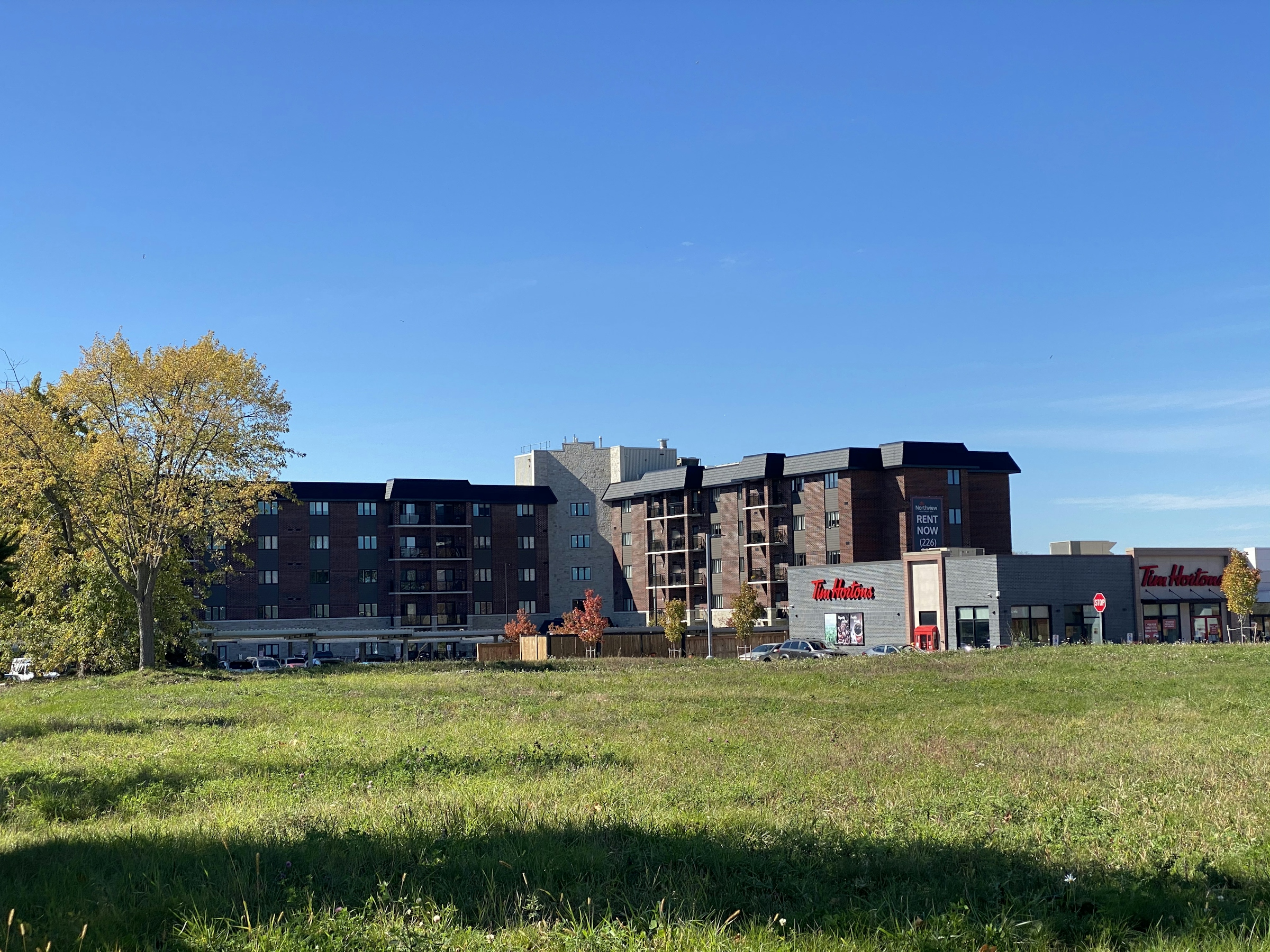 A modern multi-storey apartment building with dark cladding seen across an open grass lawn