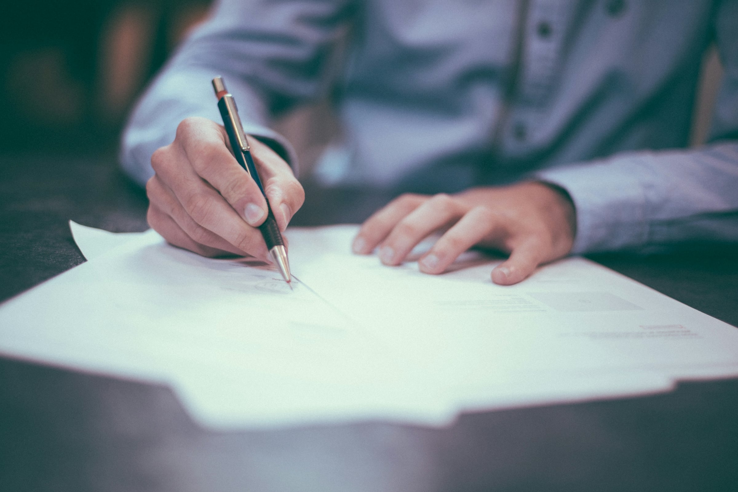 A person signing a printed document with a fountain pen on a desk