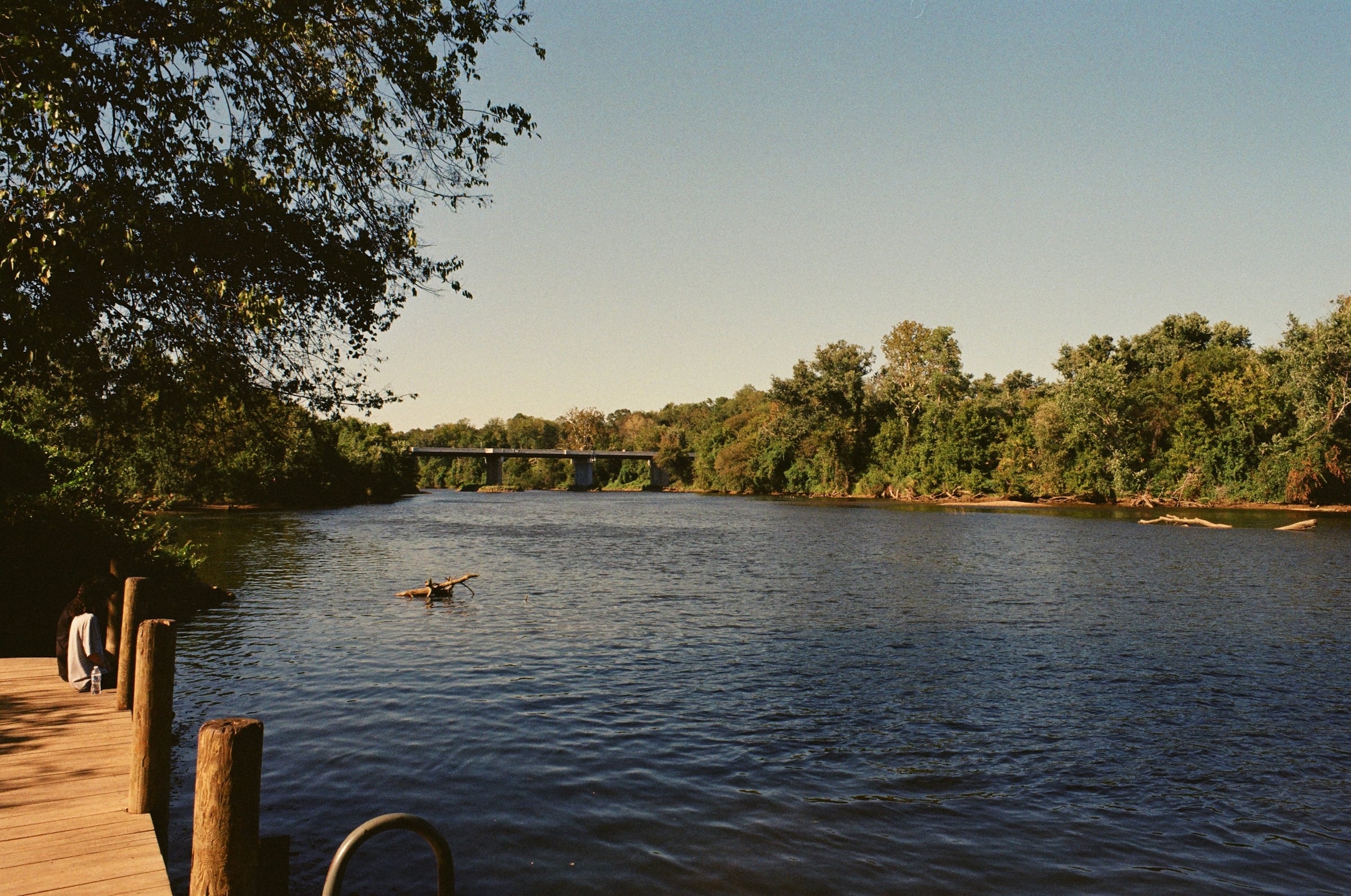 A calm river lined with trees at a small wooden dock in late afternoon light