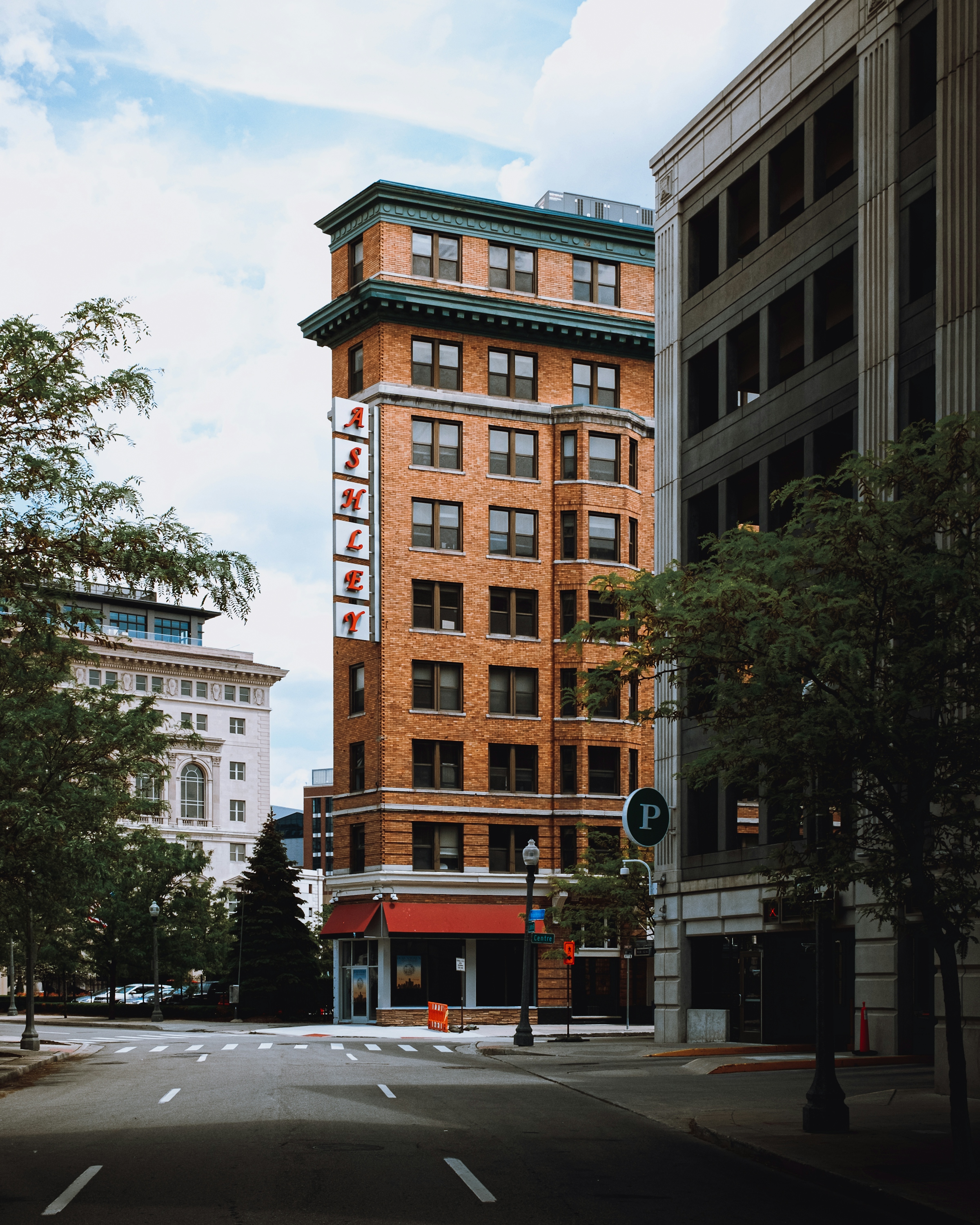 A tall brick building on a downtown corner with a vertical sign, beside a taller concrete tower.