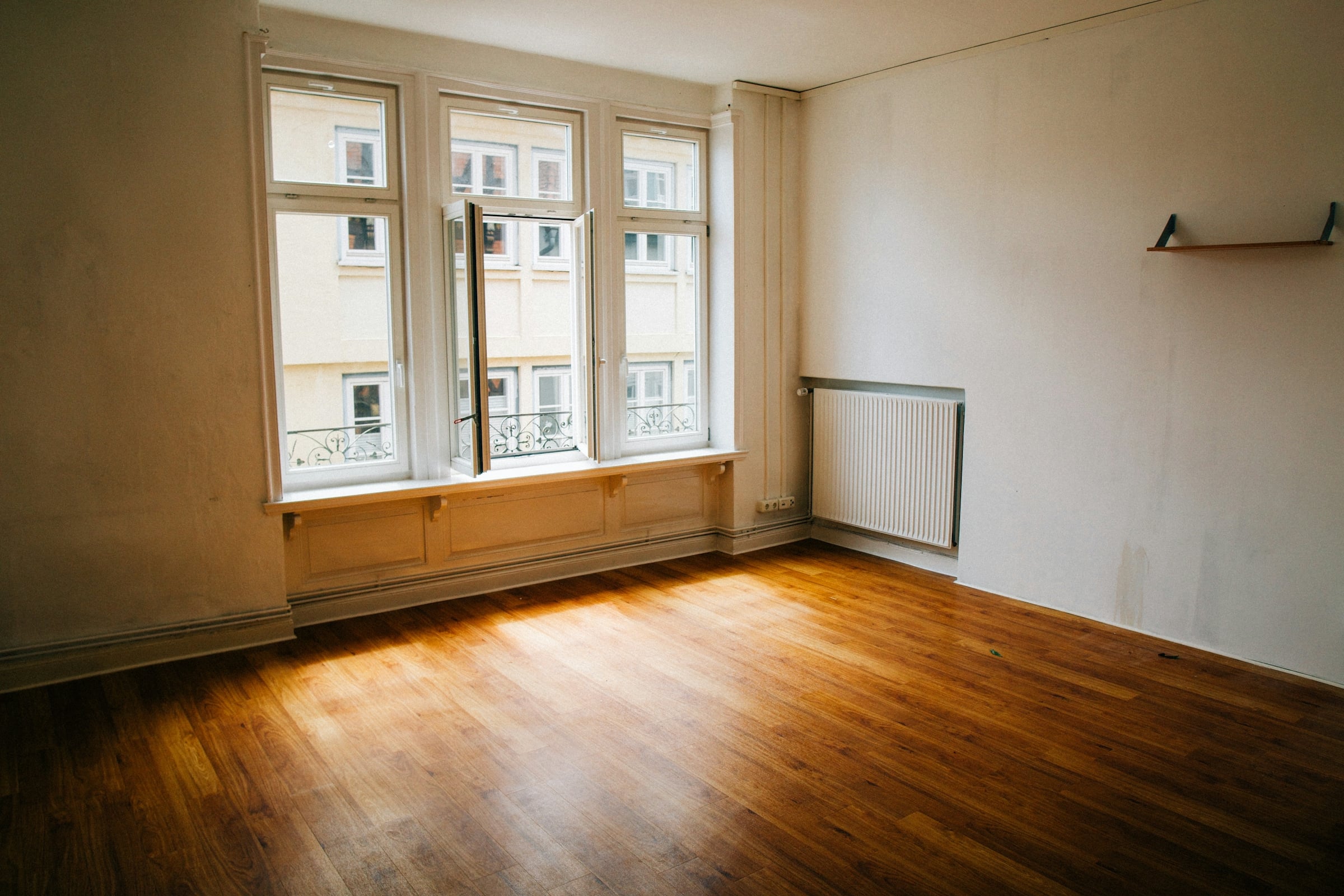 Empty room in a just-vacated house with bare hardwood floors and tall windows