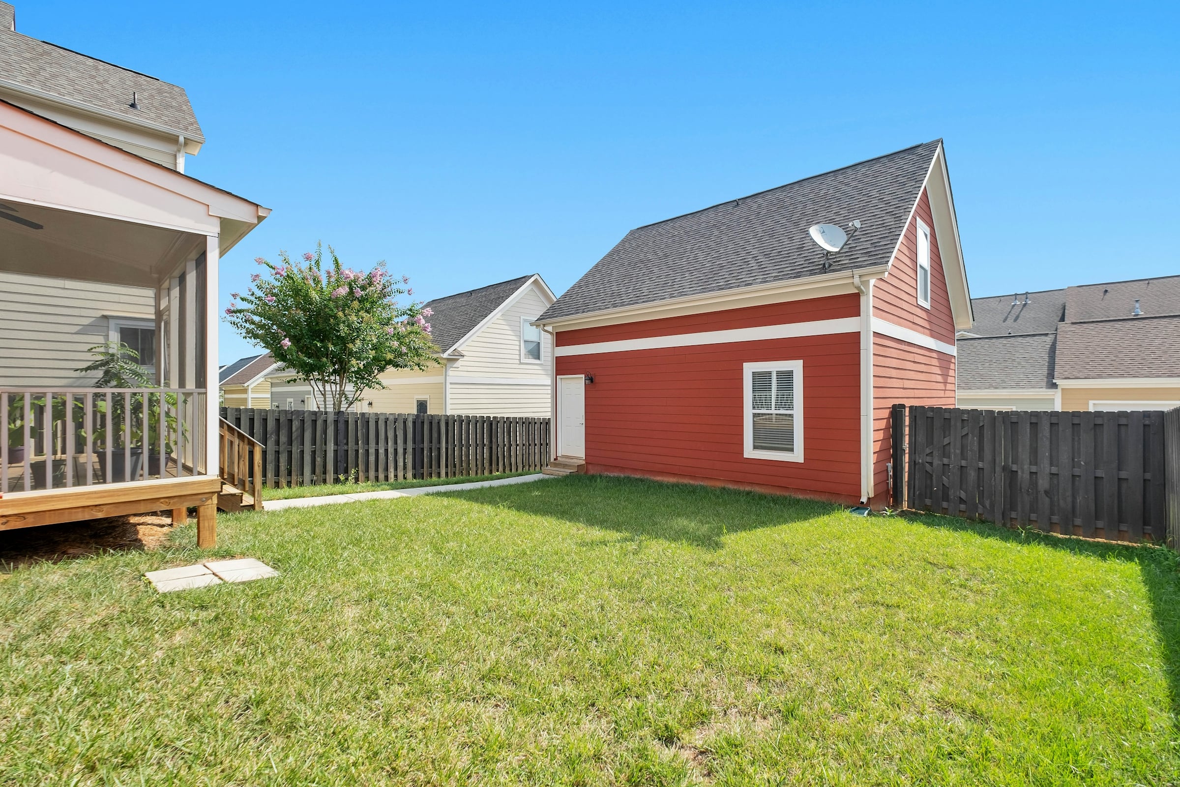 A fenced back yard with mown grass beside a red-sided detached garage, with neighboring houses behind.