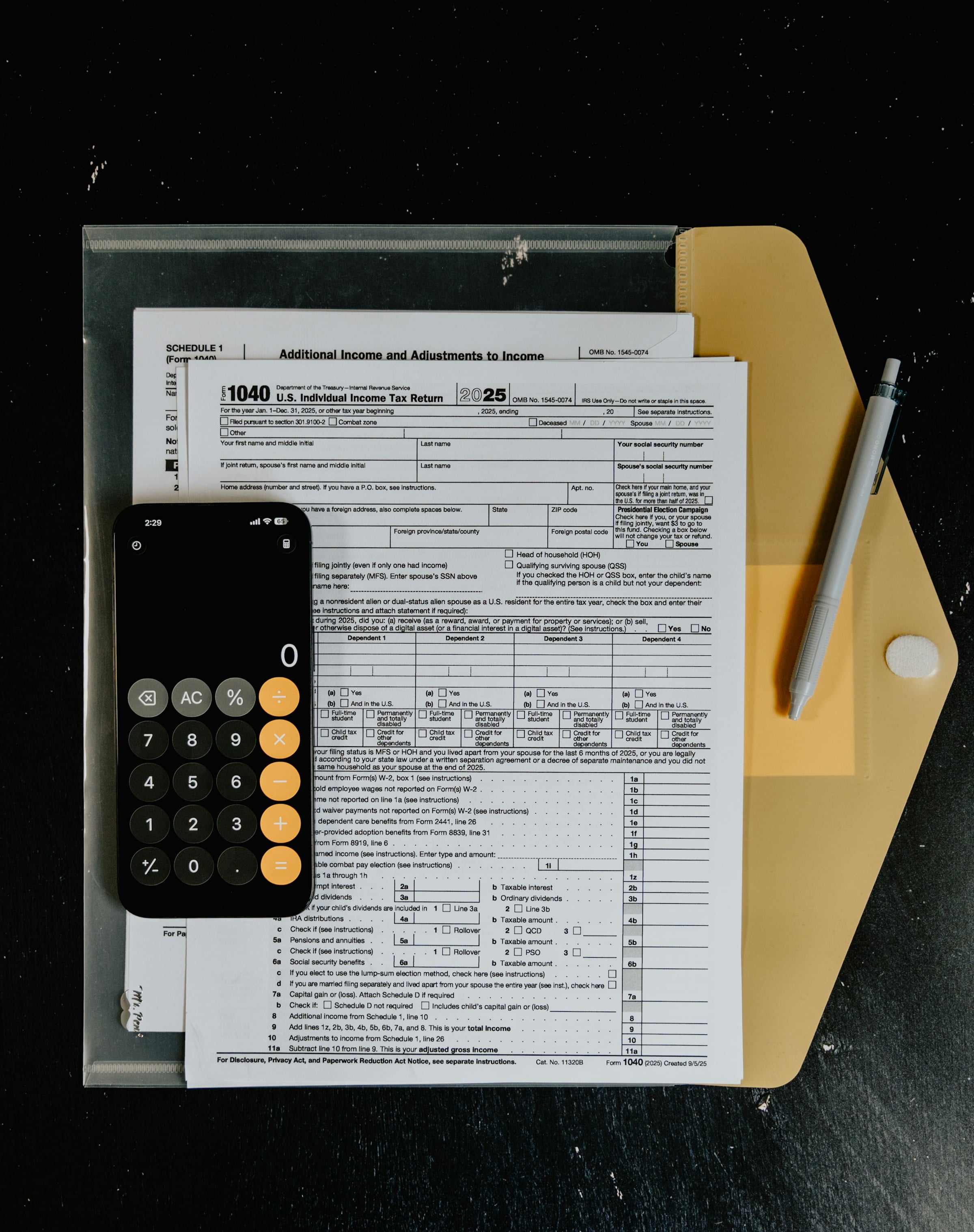 Federal Form 1040 pages with a phone calculator and pen on a tan folder