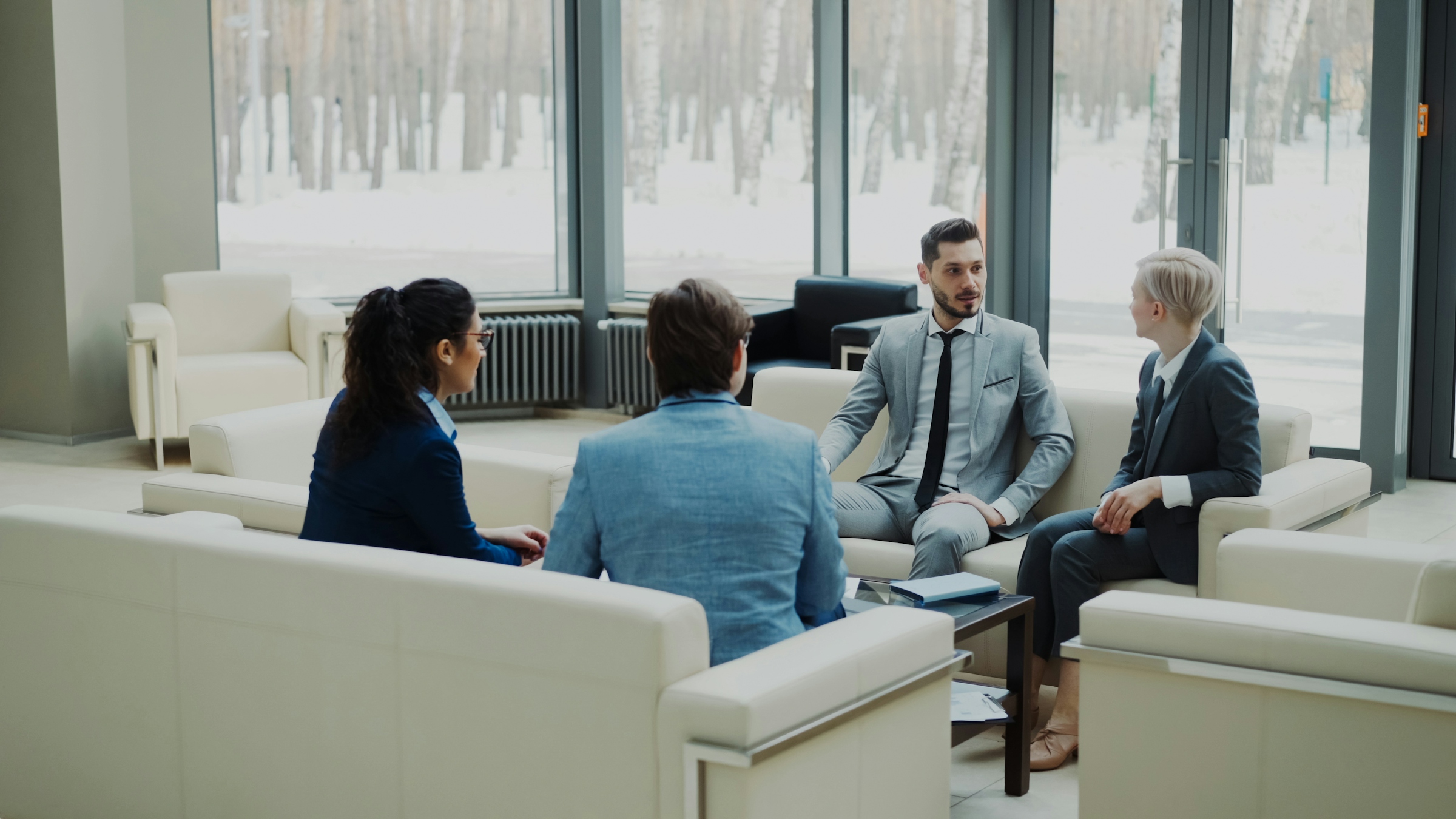 Four people seated in armchairs around a low table in a meeting room, one gesturing while speaking
