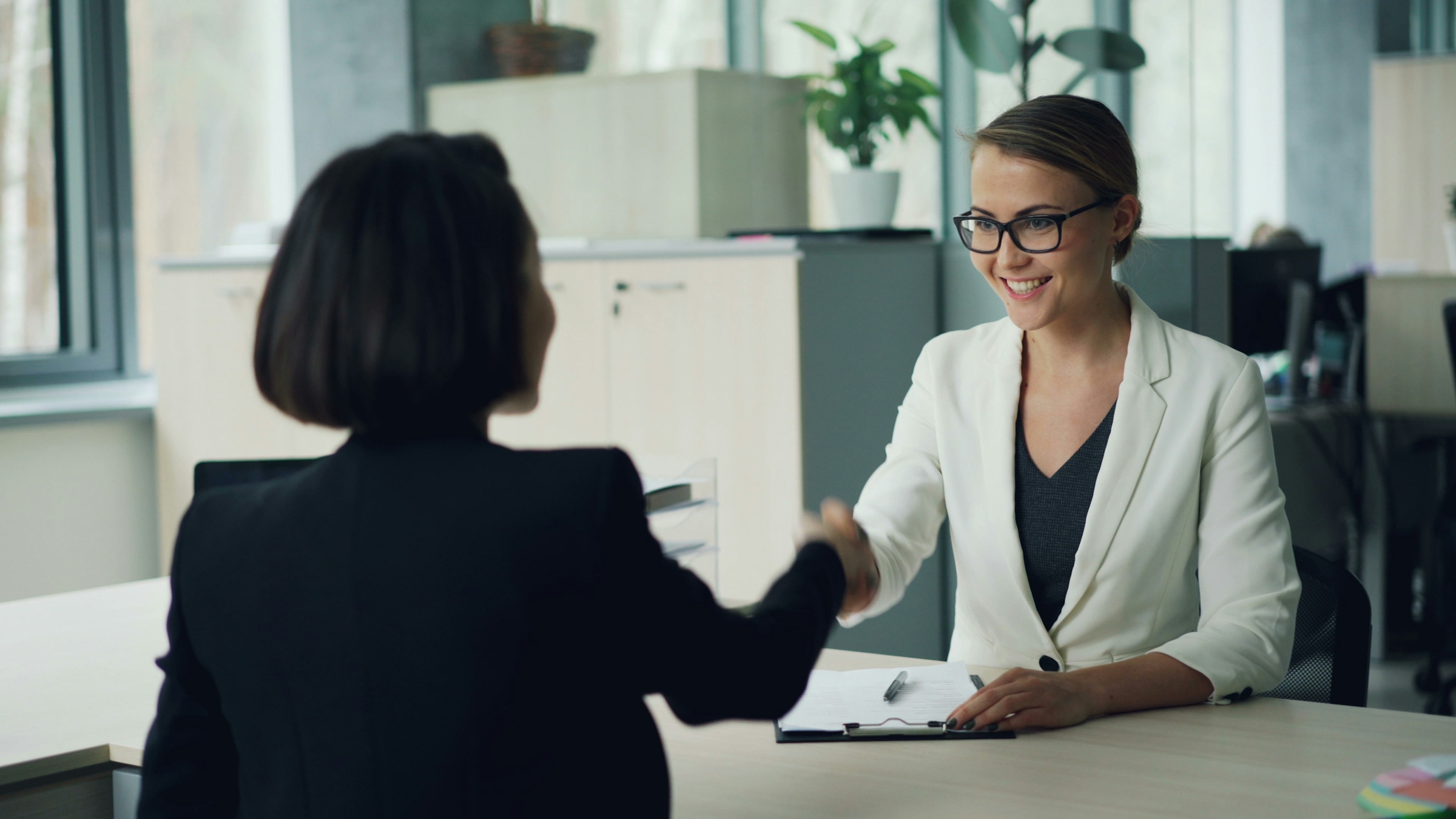 Two women shaking hands across an office desk