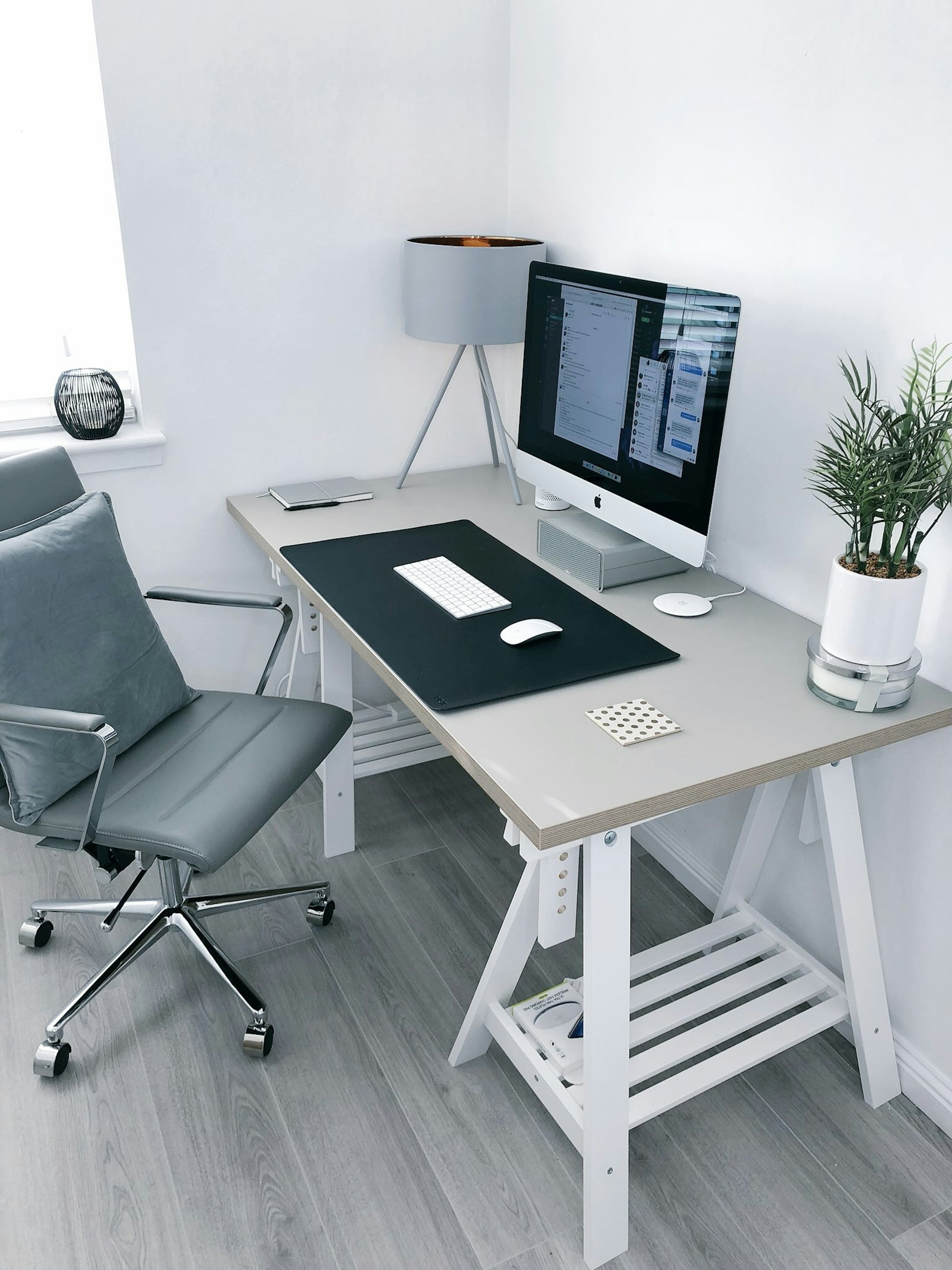 White trestle desk with a desktop computer, grey office chair and a potted plant in a bright home office