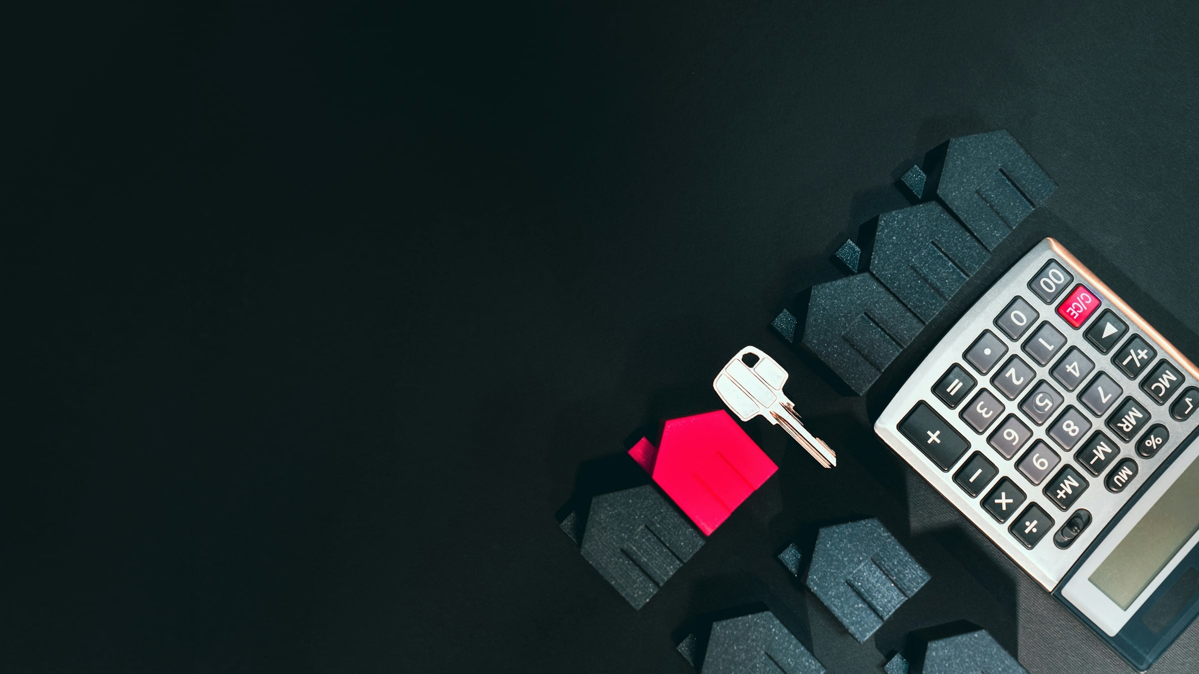 A silver key, a small red house model and a calculator arranged on a dark surface