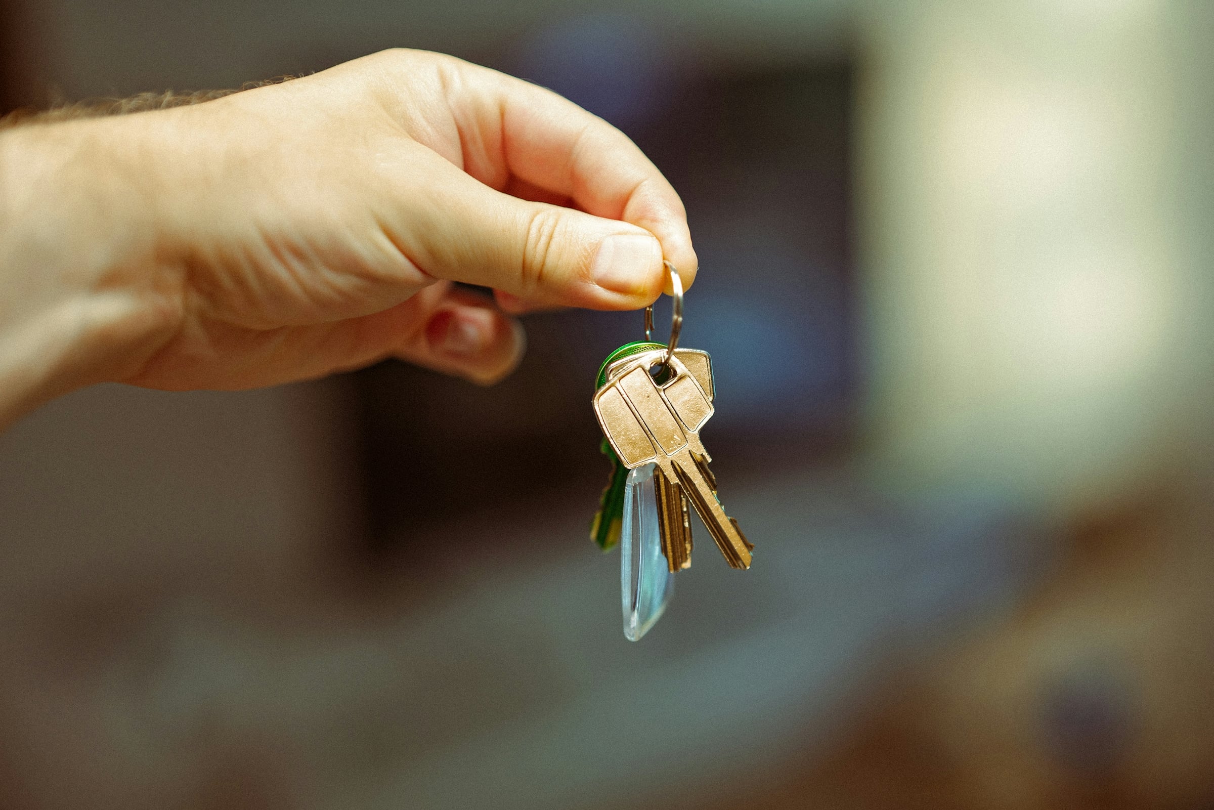 Hand holding a set of house keys on a ring against a plain pale background