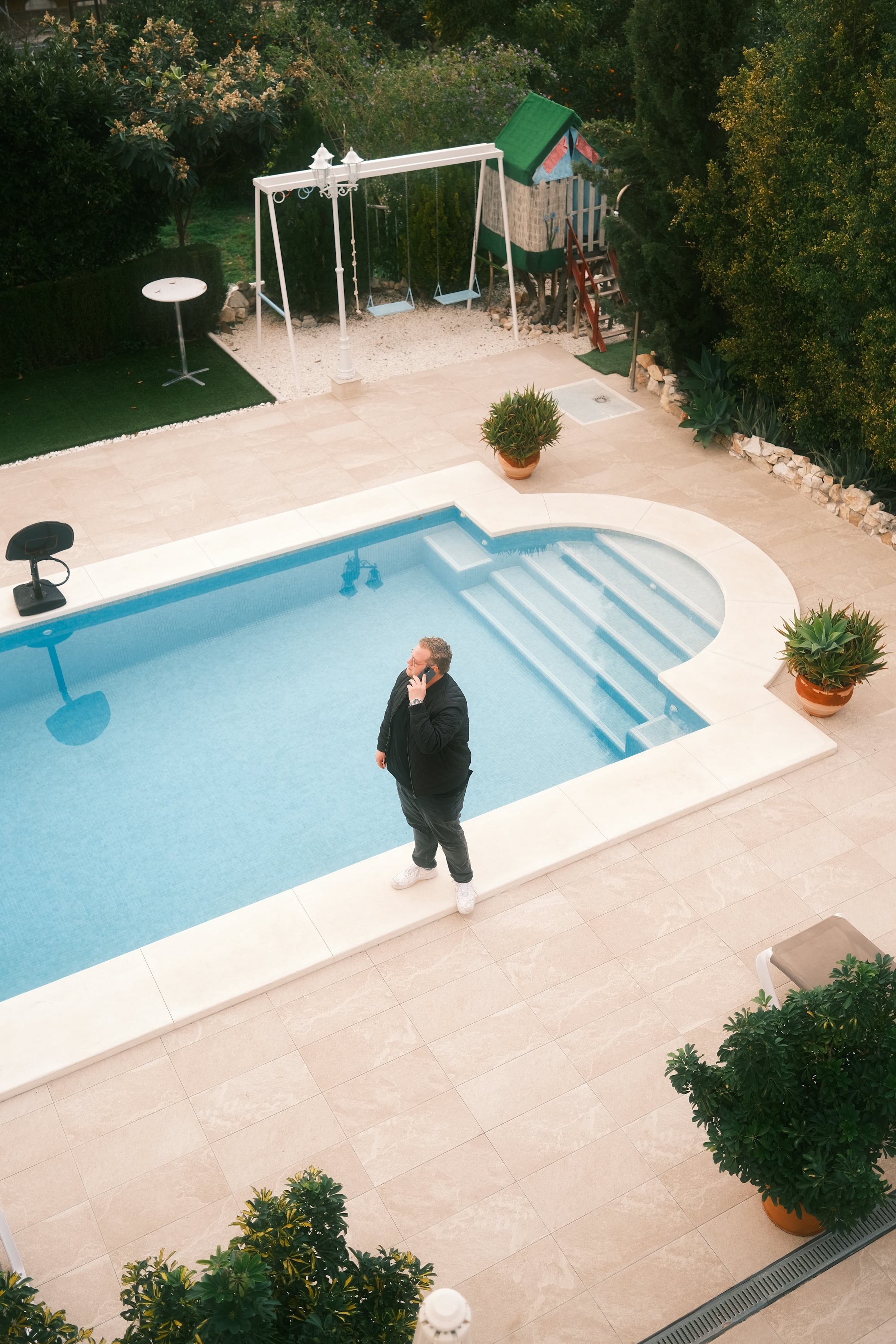 A rectangular in-ground swimming pool with a paved surround, a white pergola and clipped shrubs in a private back yard.