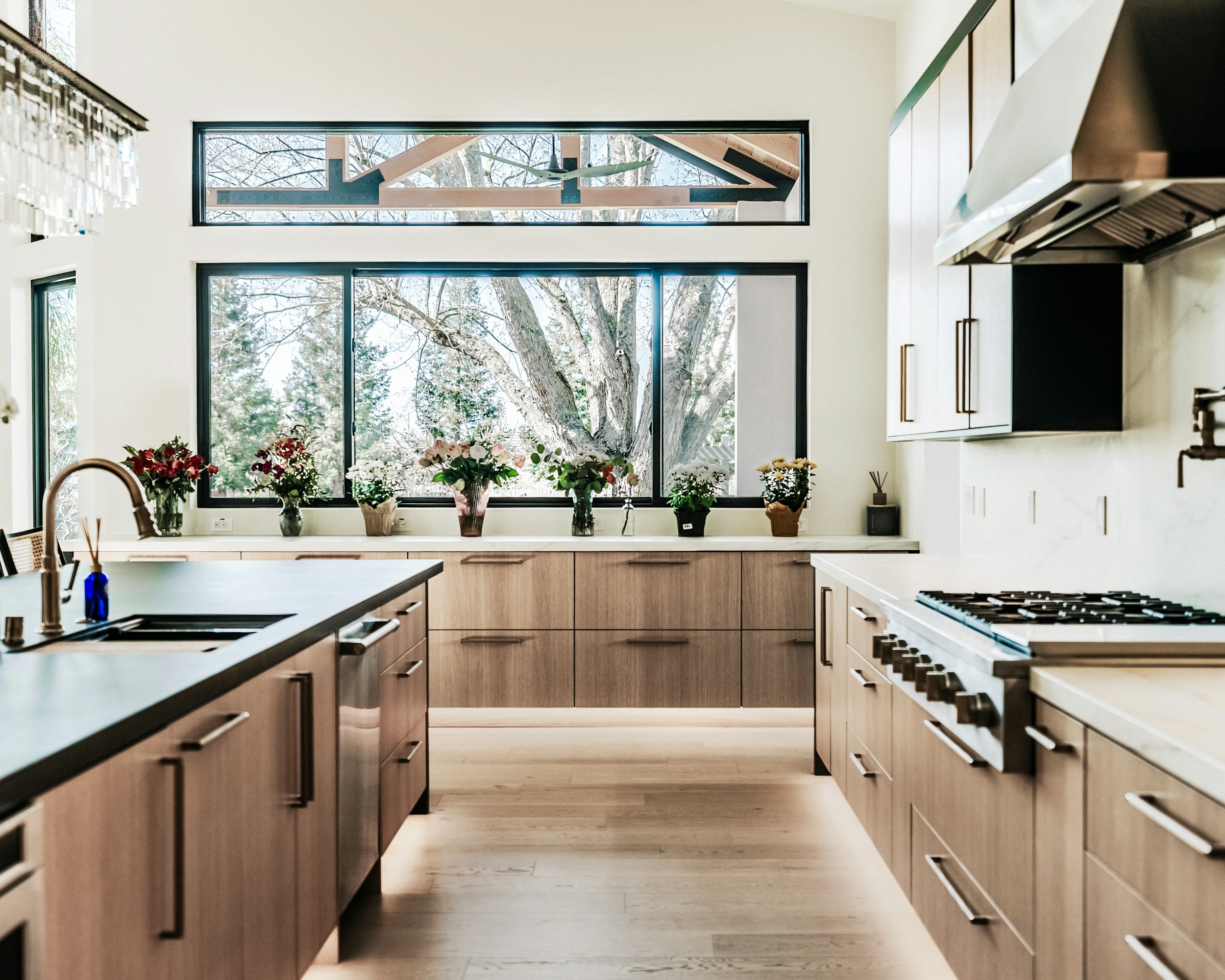 A kitchen sink beneath a wide window with potted plants along the sill