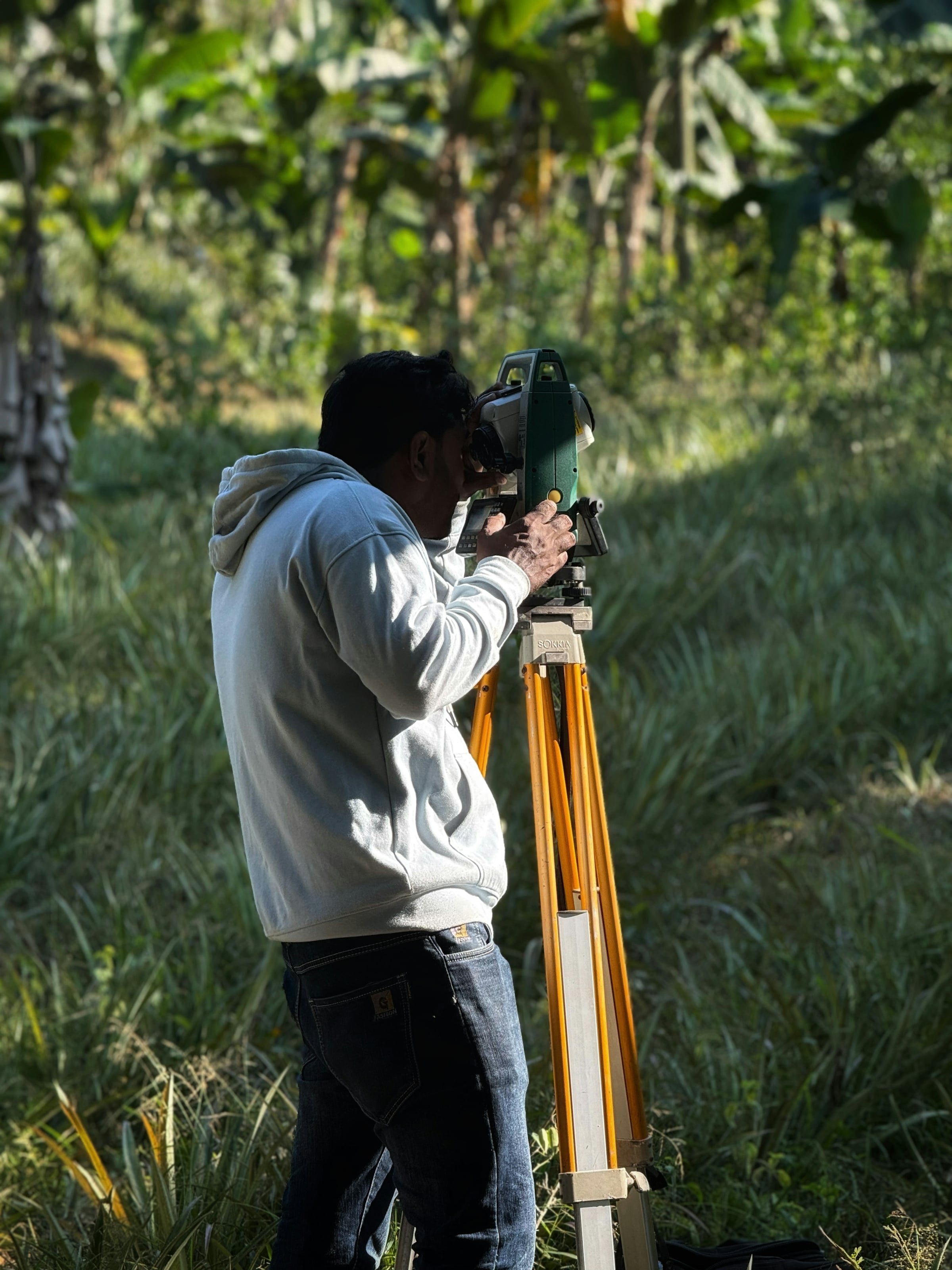 Surveyor sighting through a tripod-mounted instrument in a grassy field