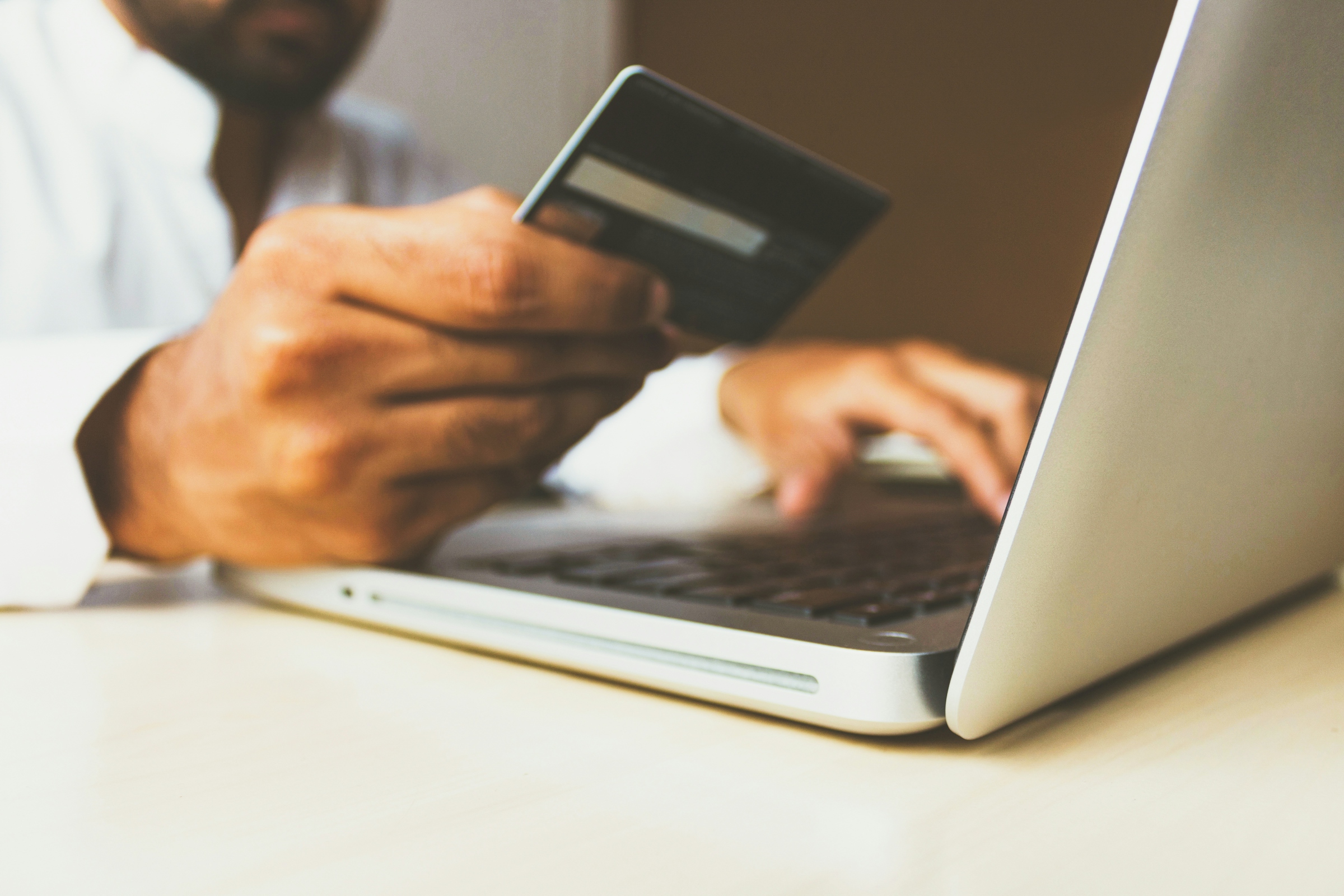 A person using a laptop while holding a payment card