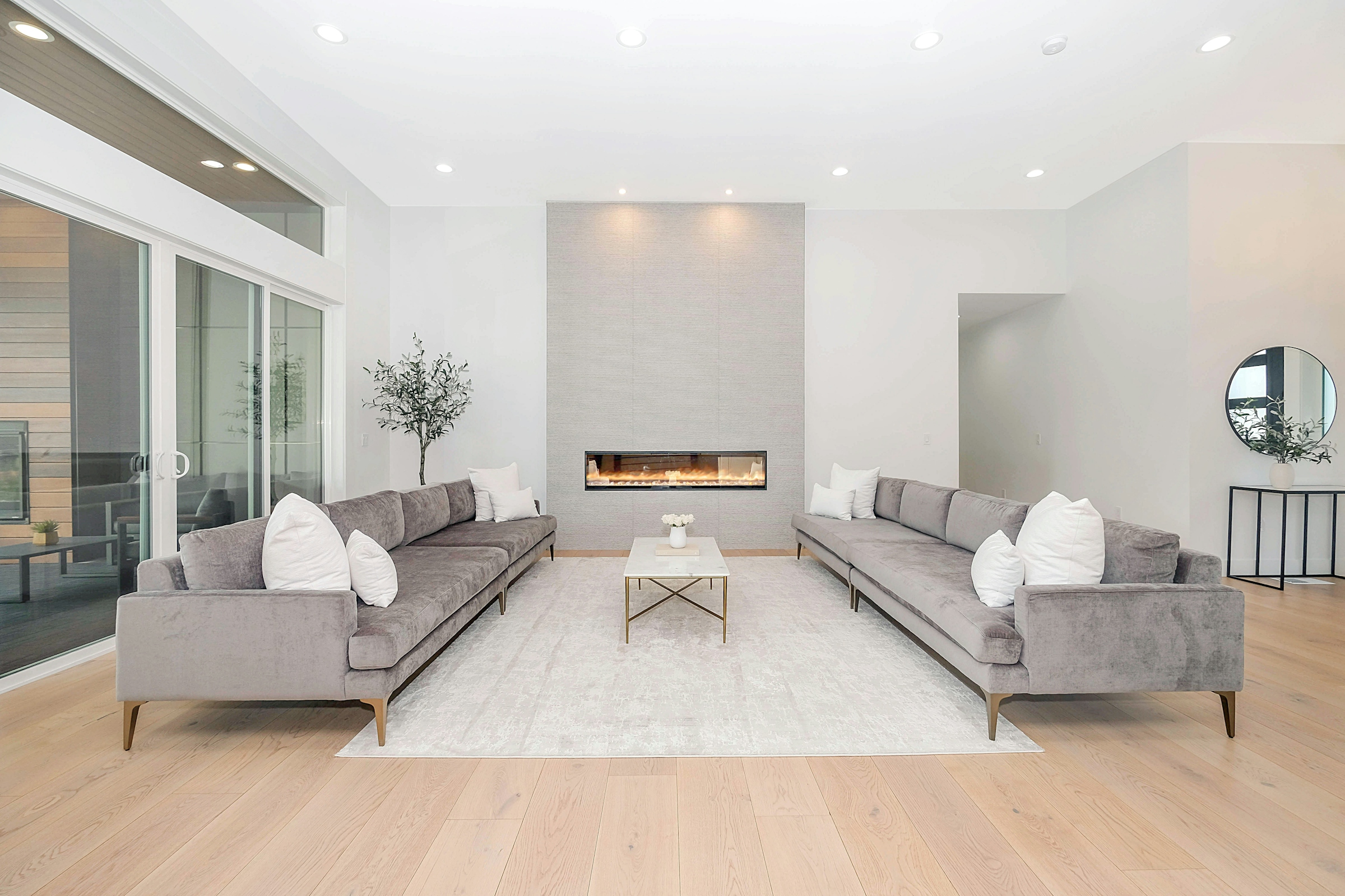 A living room with two pale grey sofas facing each other across a low table, with a long linear fireplace.