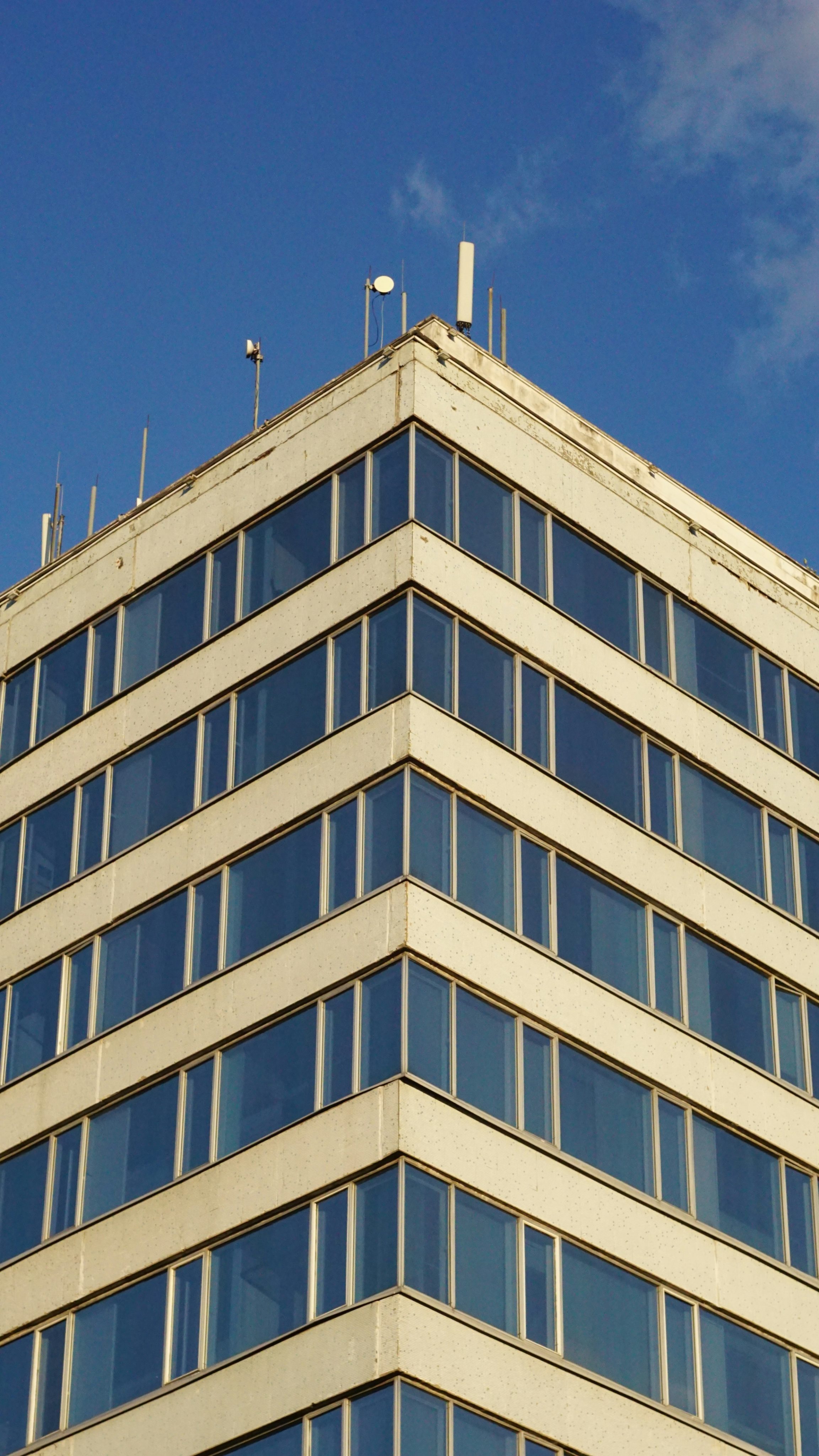 Looking up at the corner of a mid-century modern office tower with a striped facade of cream panels and blue glass windows against a clear sky.