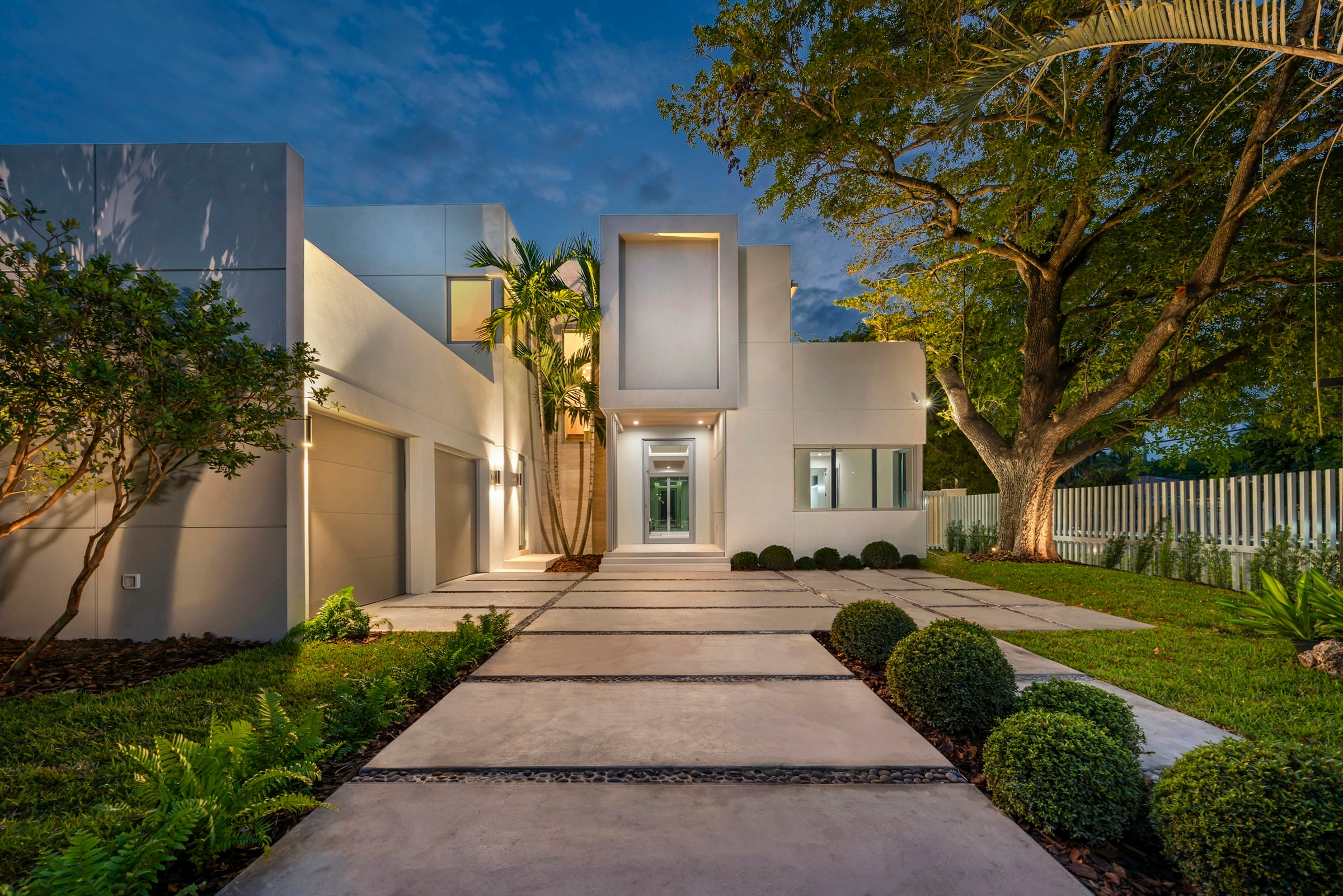 A modern two-storey home lit at dusk, with a landscaped walkway leading to the front entrance.