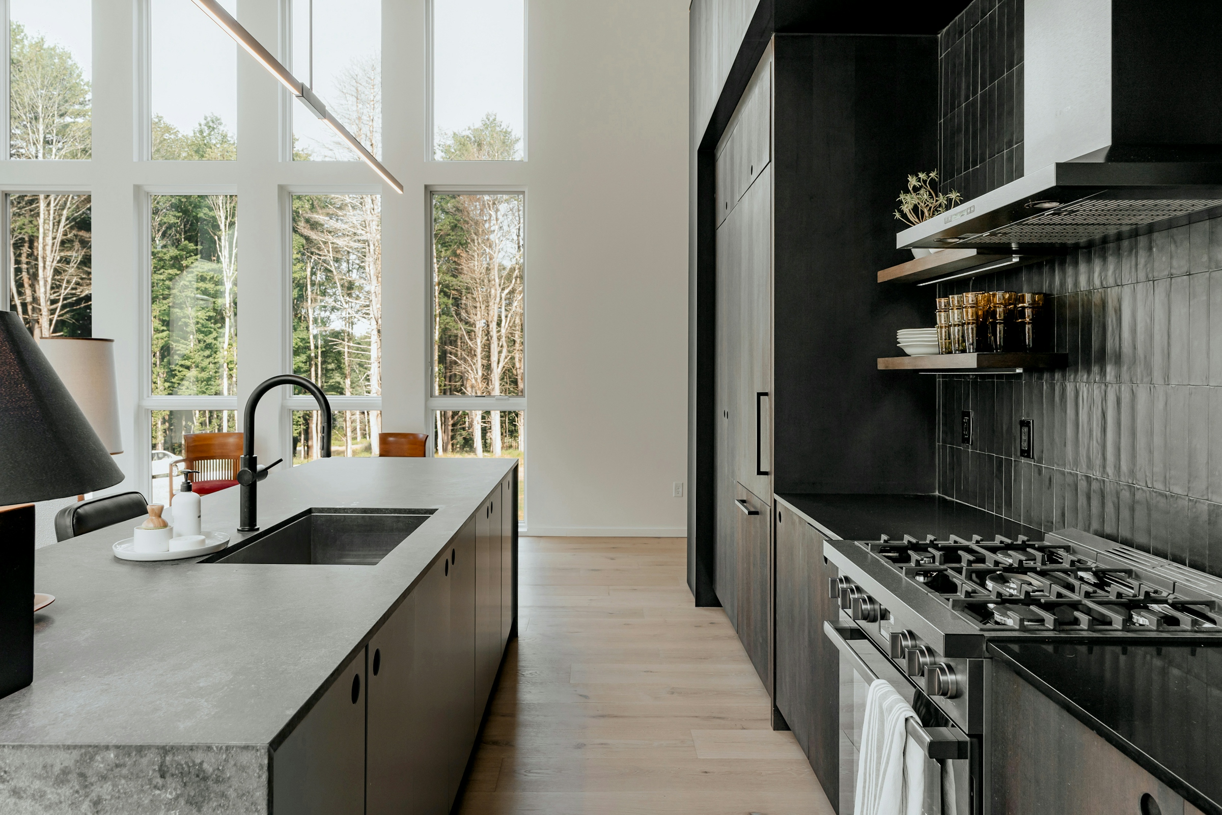 A modern kitchen with dark cabinetry, a stone worktop and tall windows along one wall