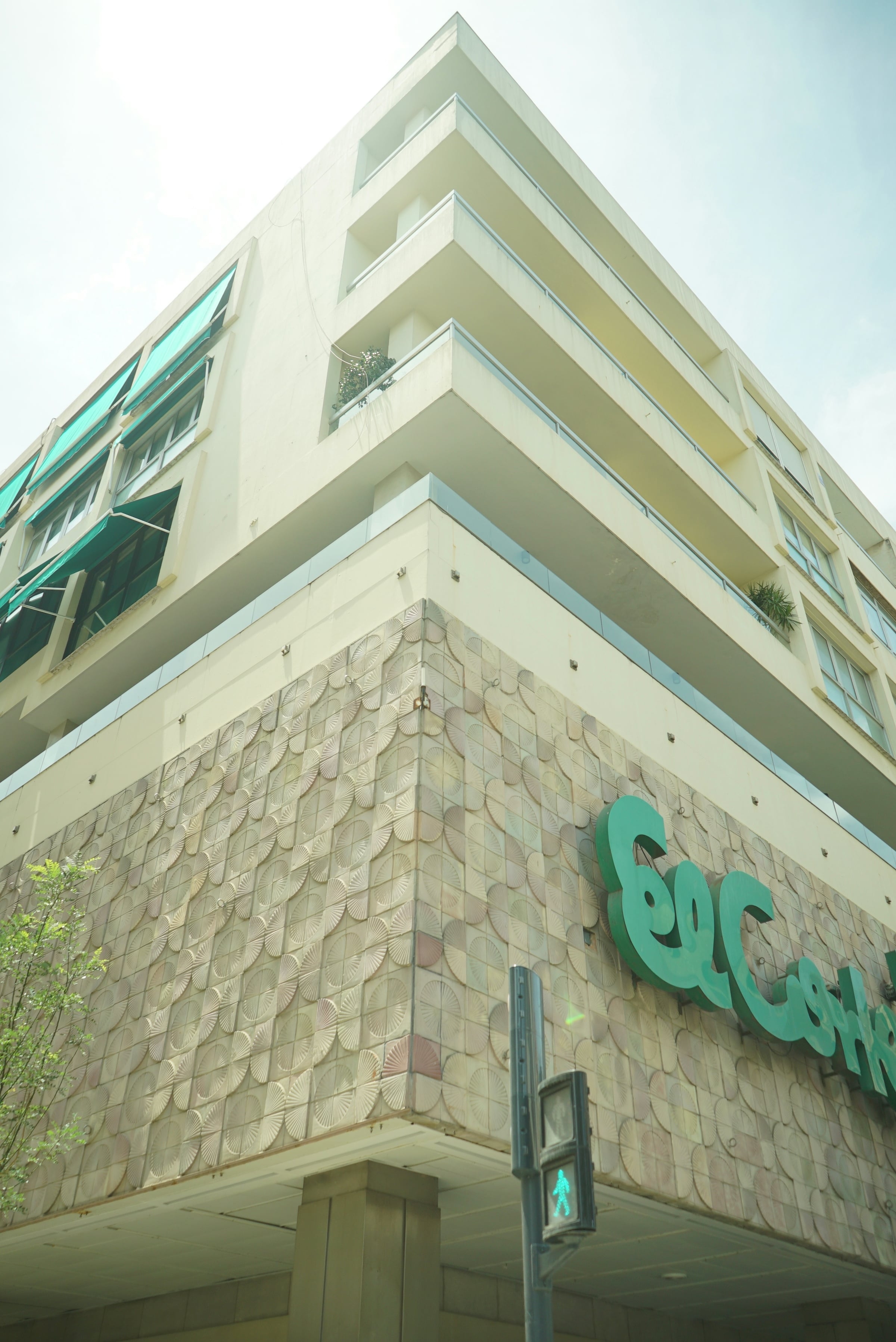 The corner of a modern retail building clad in pale textured panels, with green signage above the entrance.