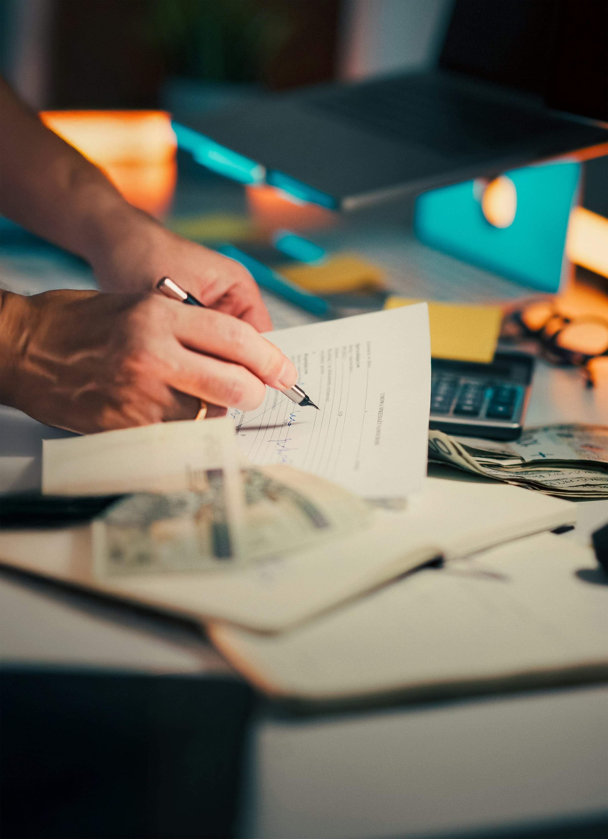 A hand filling in a loan document at a desk with a calculator and US banknotes alongside