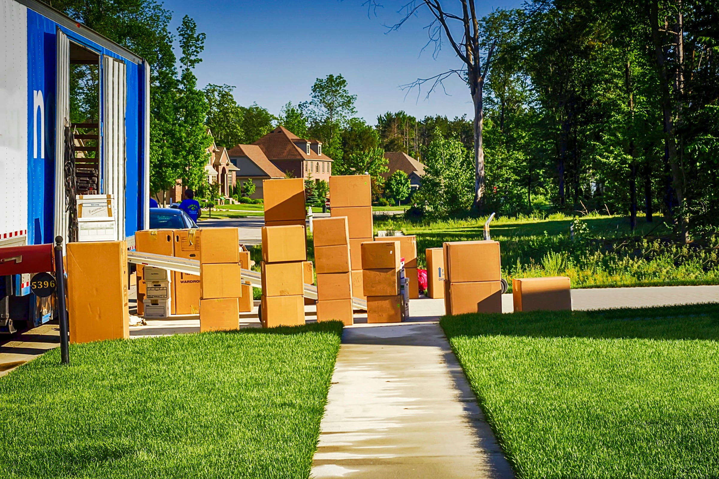 Open moving truck with stacked cardboard boxes on the front lawn of a house