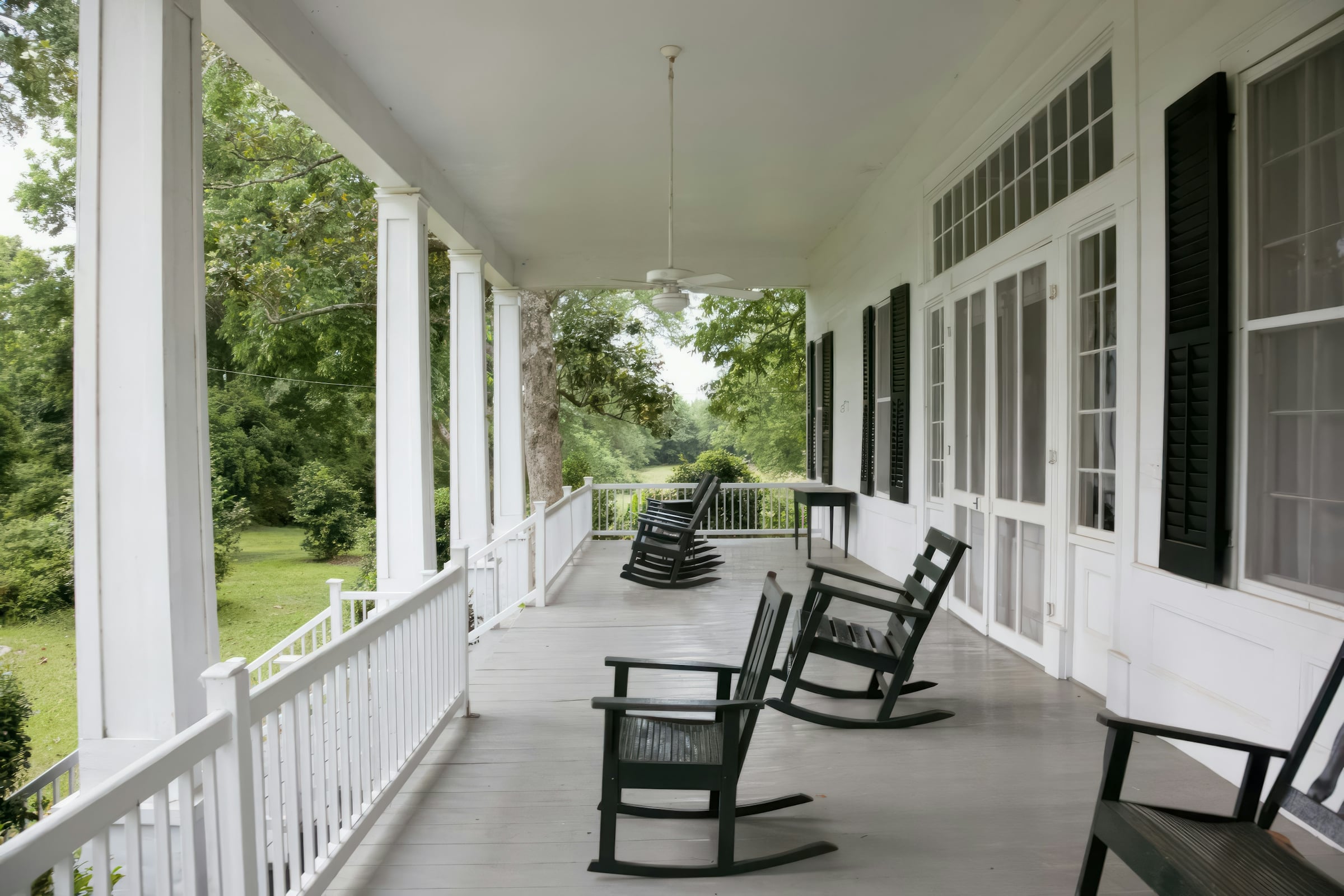Covered front porch with white columns and wooden rocking chairs overlooking a green lawn