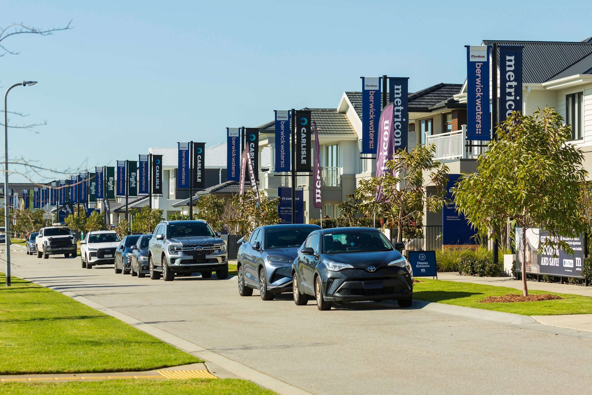 A street of newly built townhouses lined with marketing flags and parked cars in a new development