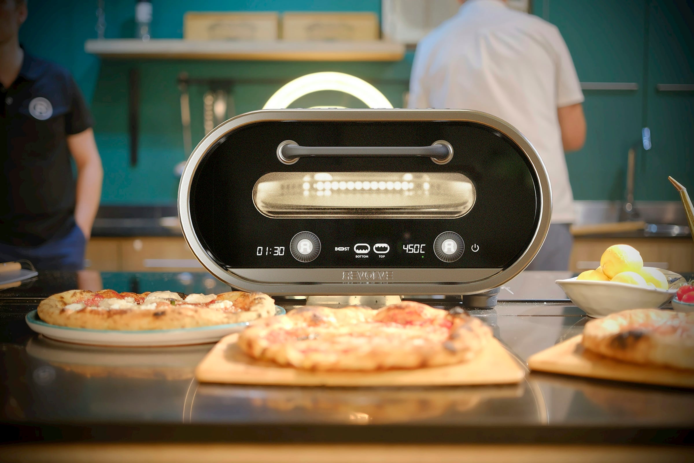 Two finished pizzas on a counter in front of a countertop pizza oven