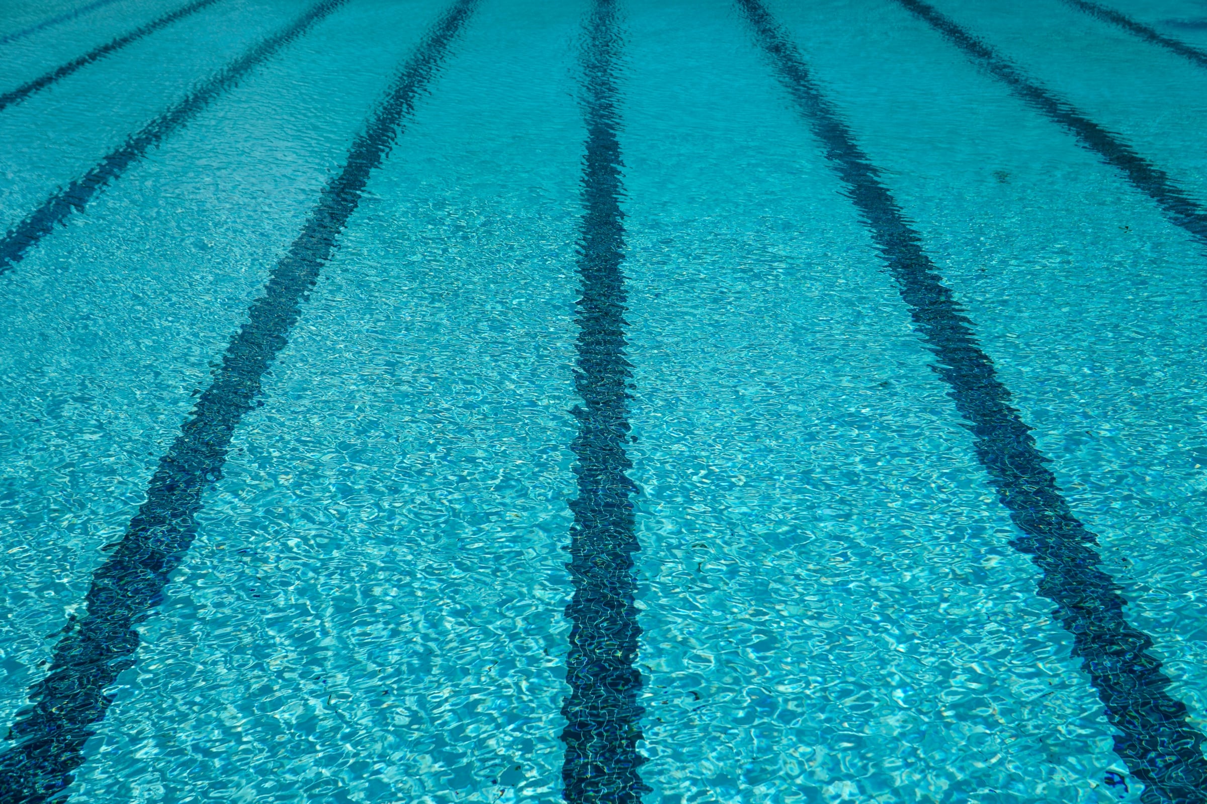 Lane ropes stretched across the clear blue water of an empty outdoor swimming pool.