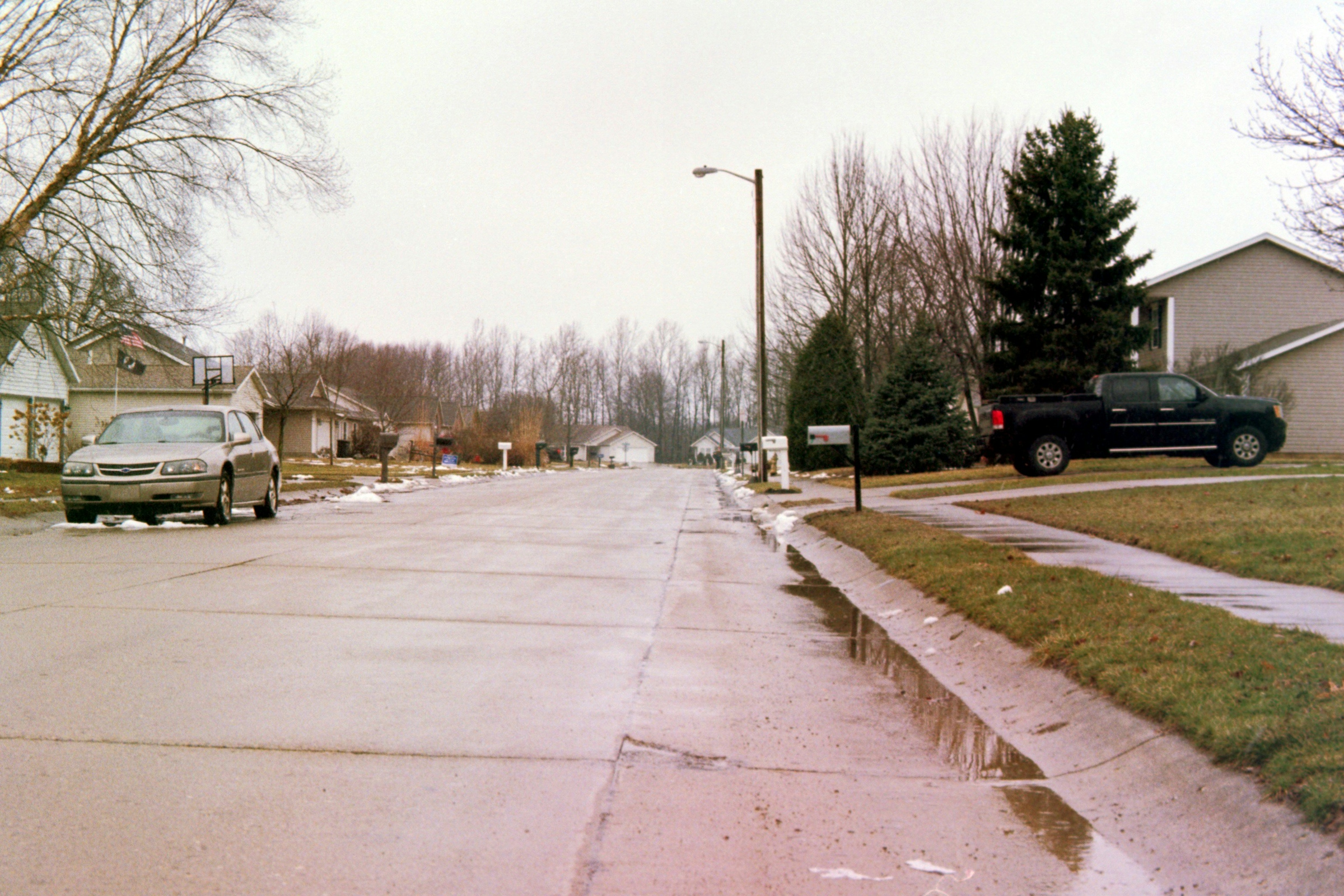A quiet residential street with pickup trucks parked at the kerb and low houses set back behind grass