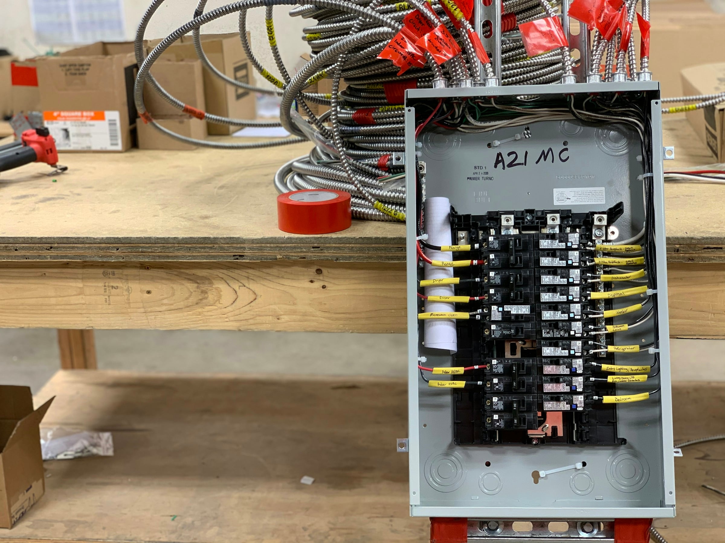 Open residential circuit breaker panel with labeled wires sitting on a plywood workbench