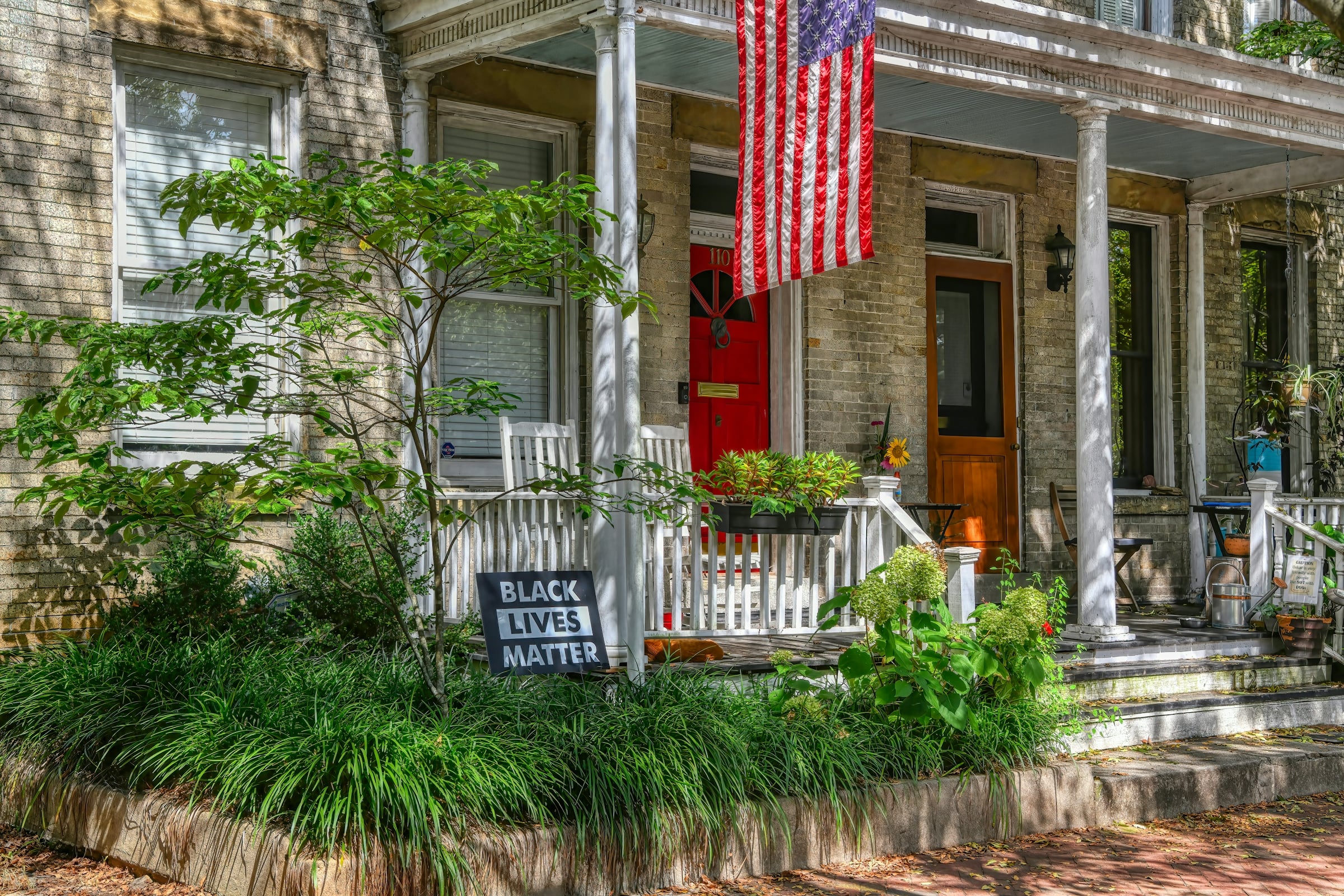 A row of covered front porches with an American flag and climbing greenery along the railings