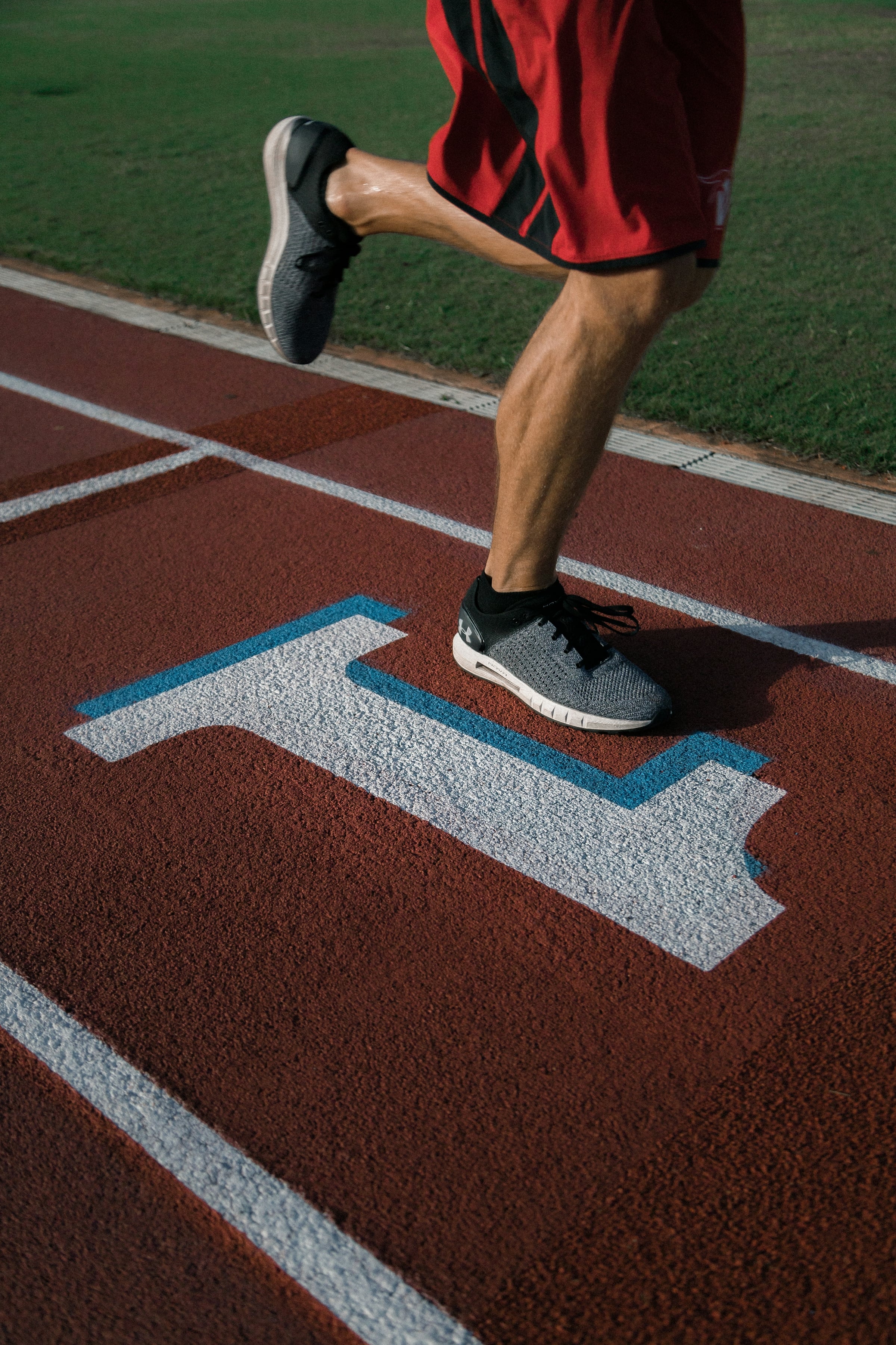 A runner's legs mid-stride on a red synthetic running track marked with white and blue lane lines.