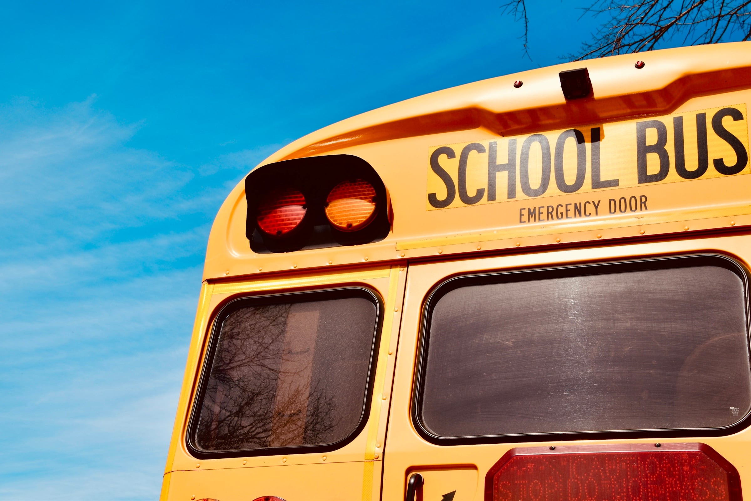 Rear of a yellow school bus with stop lights against a clear blue sky