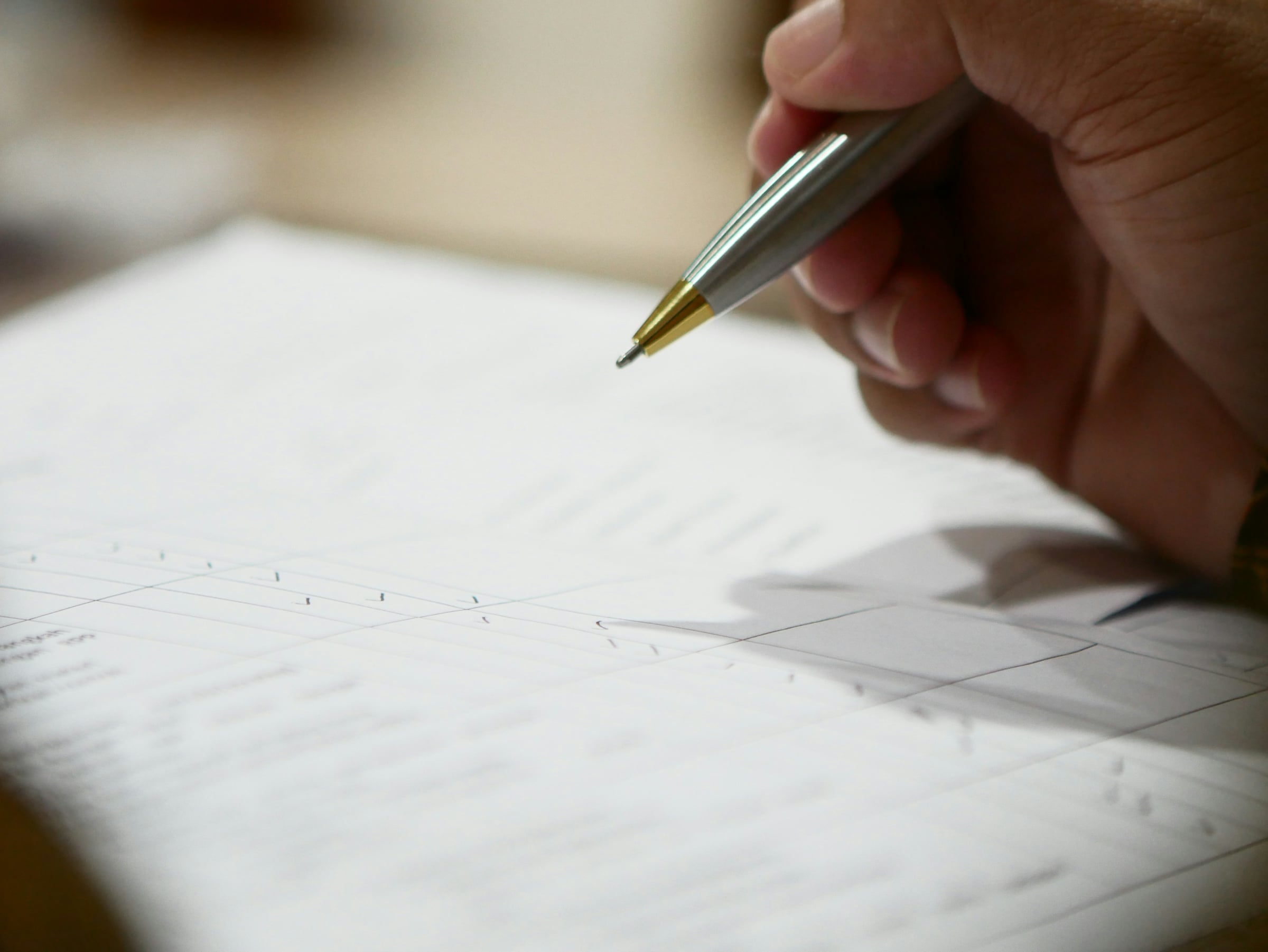 A hand holding a slim pen above a sheet of printed paper on a desk, part way through a signature.