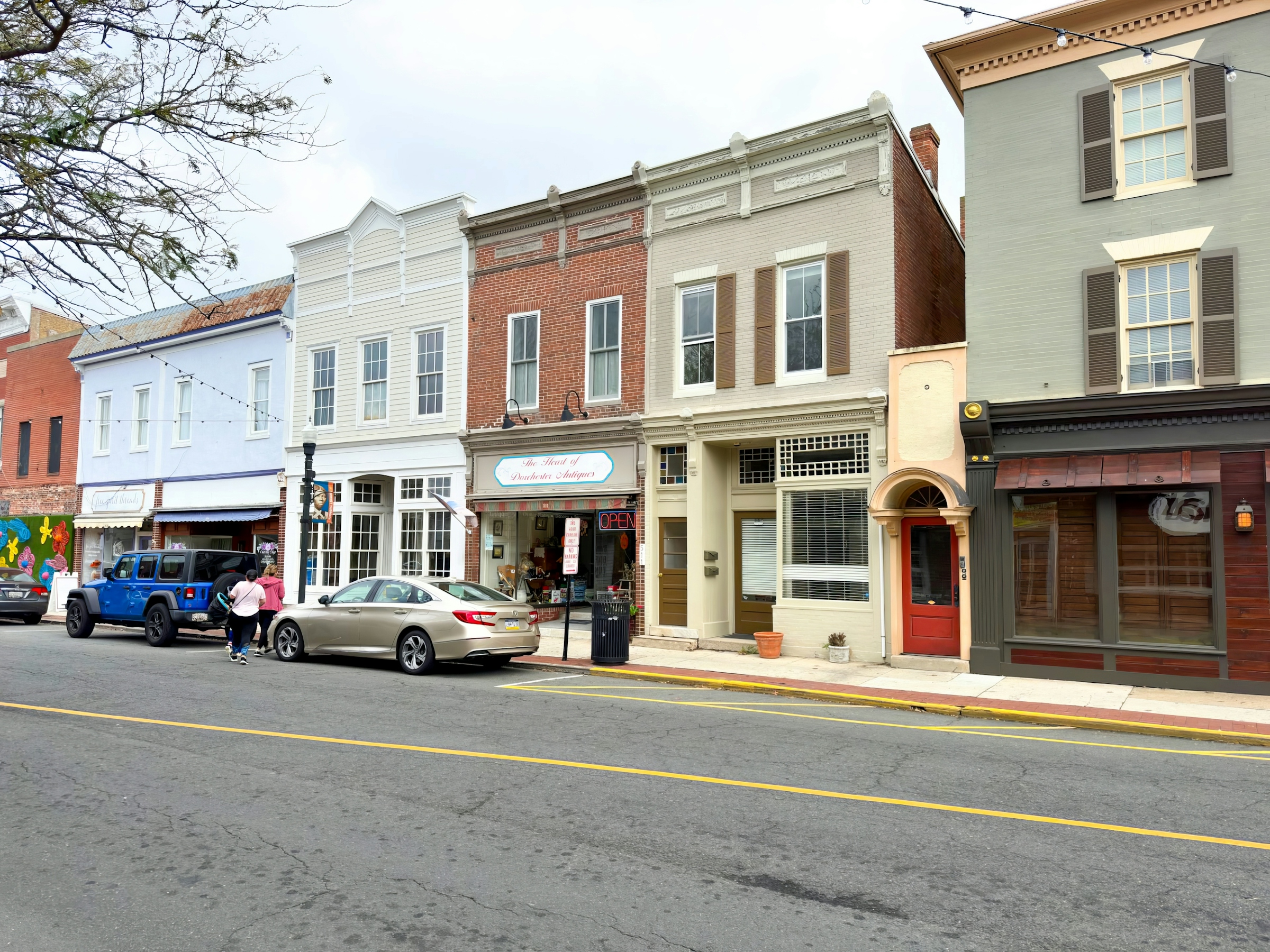 A small-town main street lined with two-storey brick storefronts and cars parked along the curb.