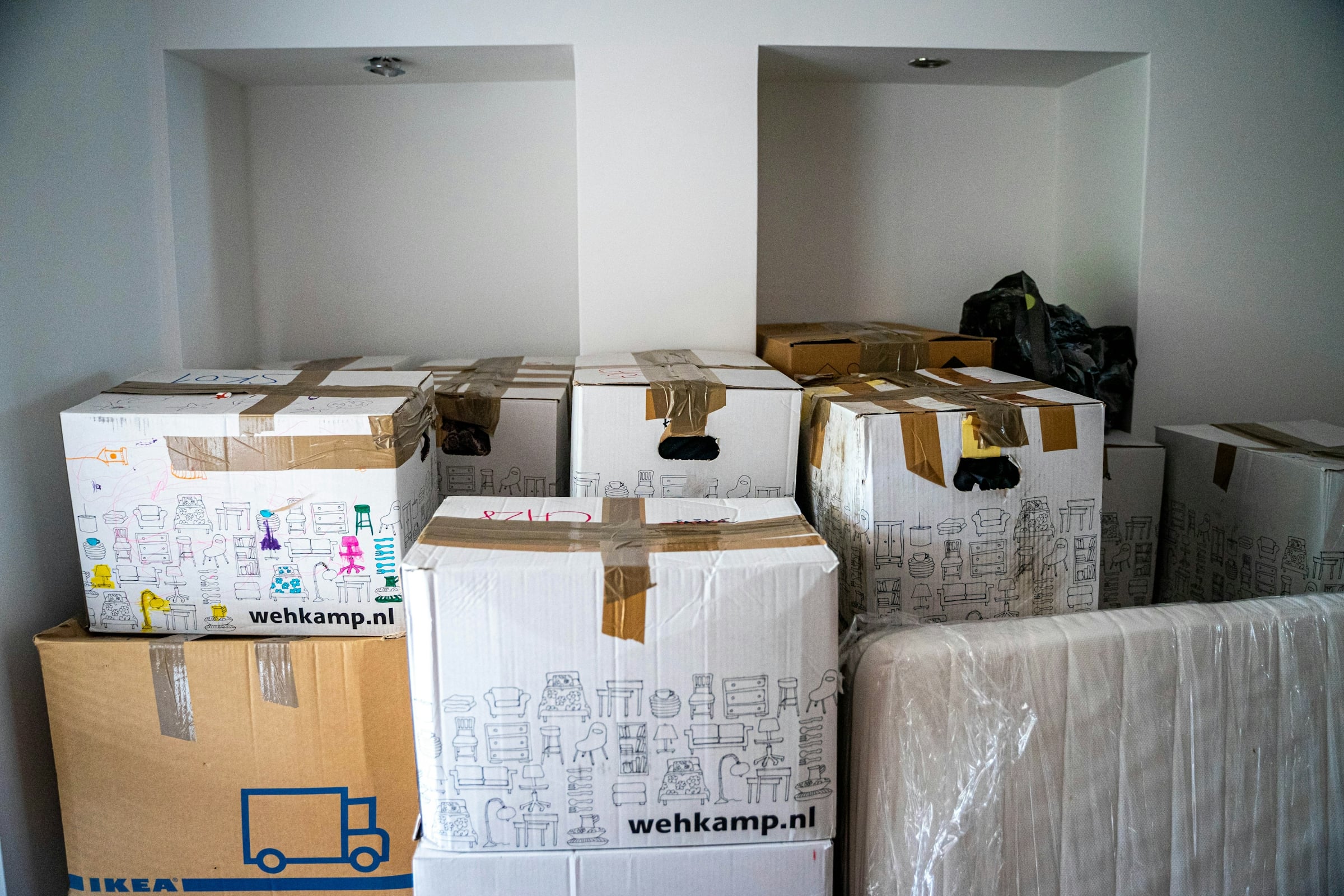 Stacked cardboard moving boxes and furniture wrapped in protective plastic in an empty room