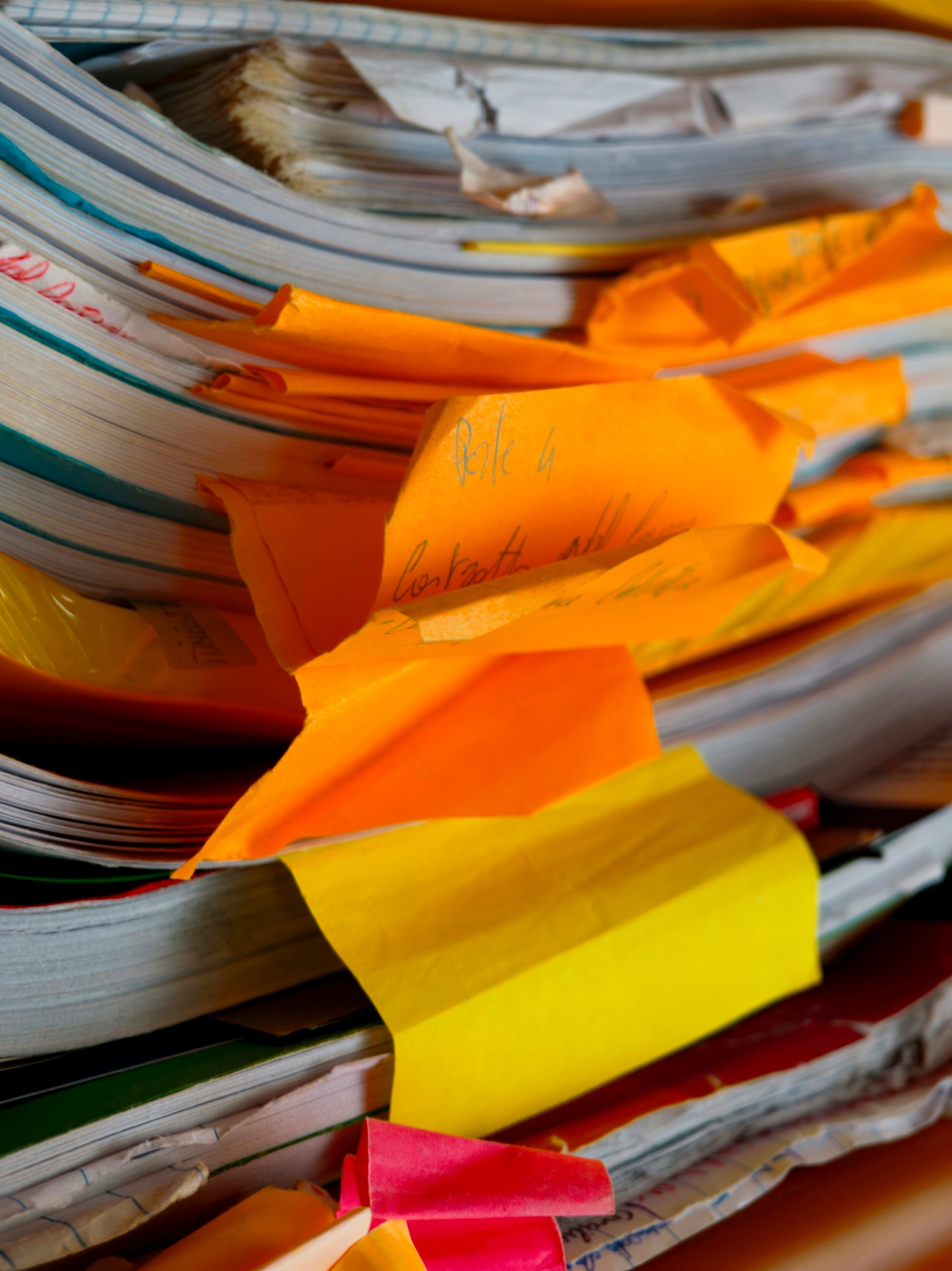 A thick stack of paper documents on a desk, interleaved with orange and yellow index tabs.