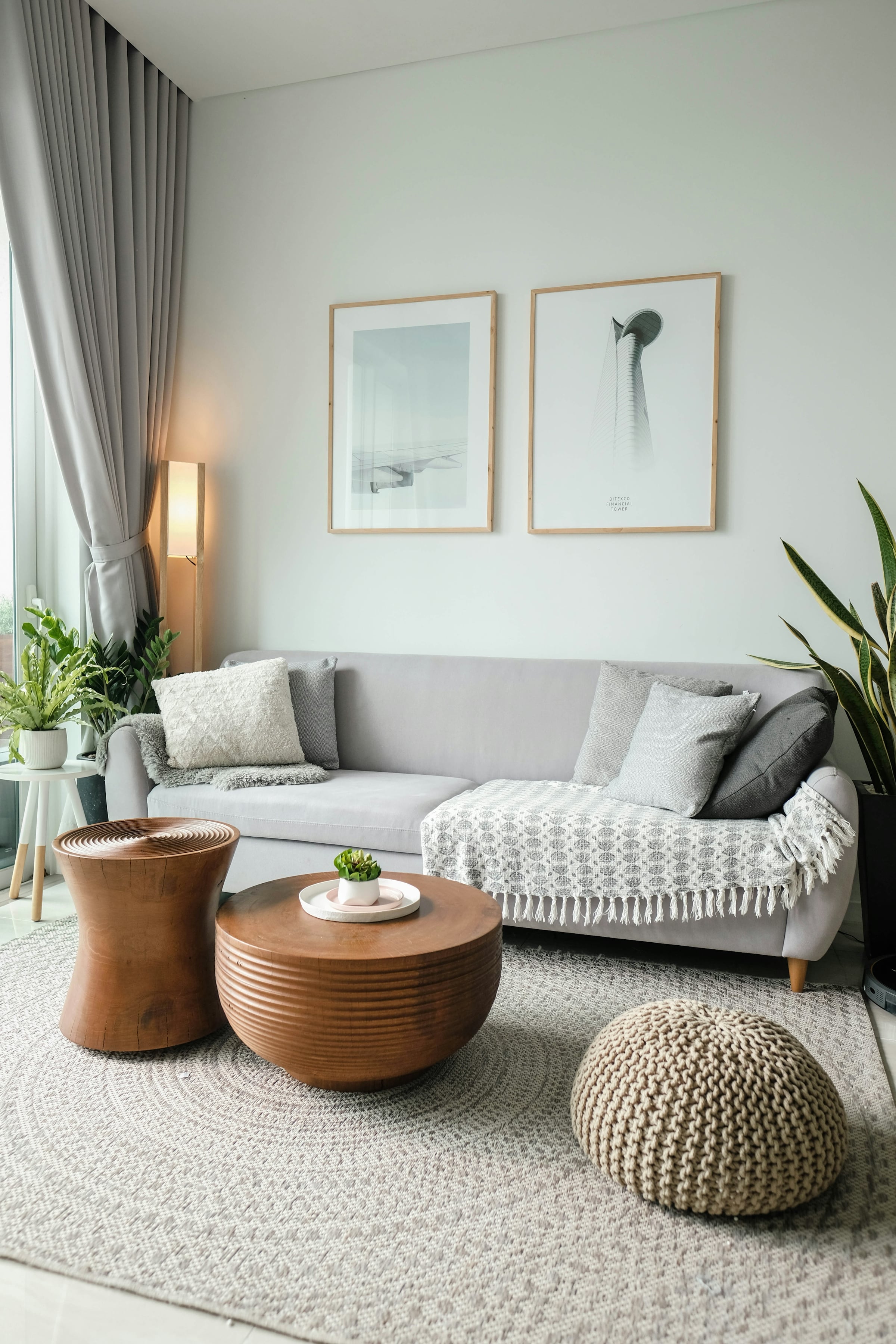 A living room staged with a pale grey sofa, layered cushions and a potted plant in the corner.