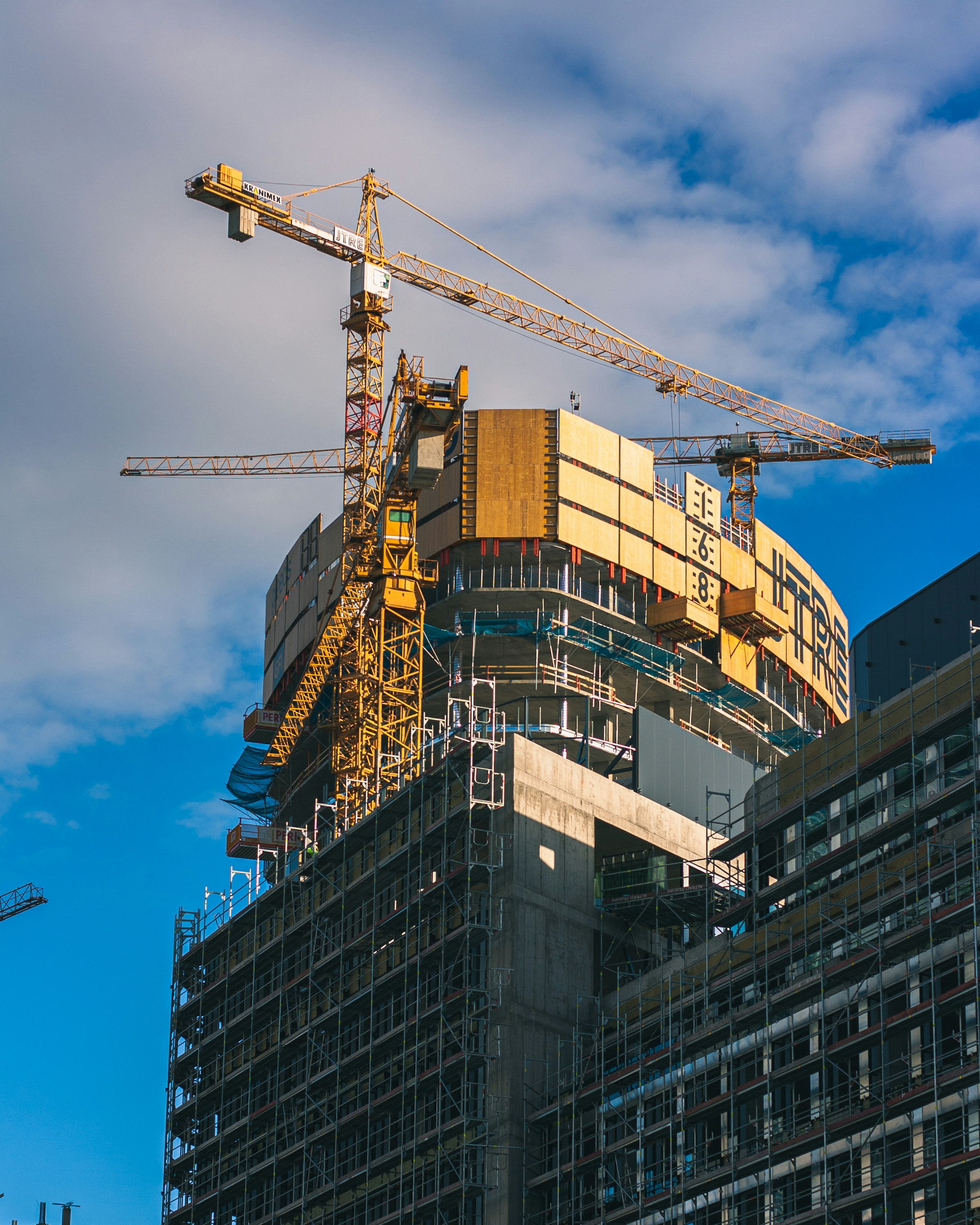A yellow tower crane standing over a partly built multi-story building against a blue sky with scattered cloud.