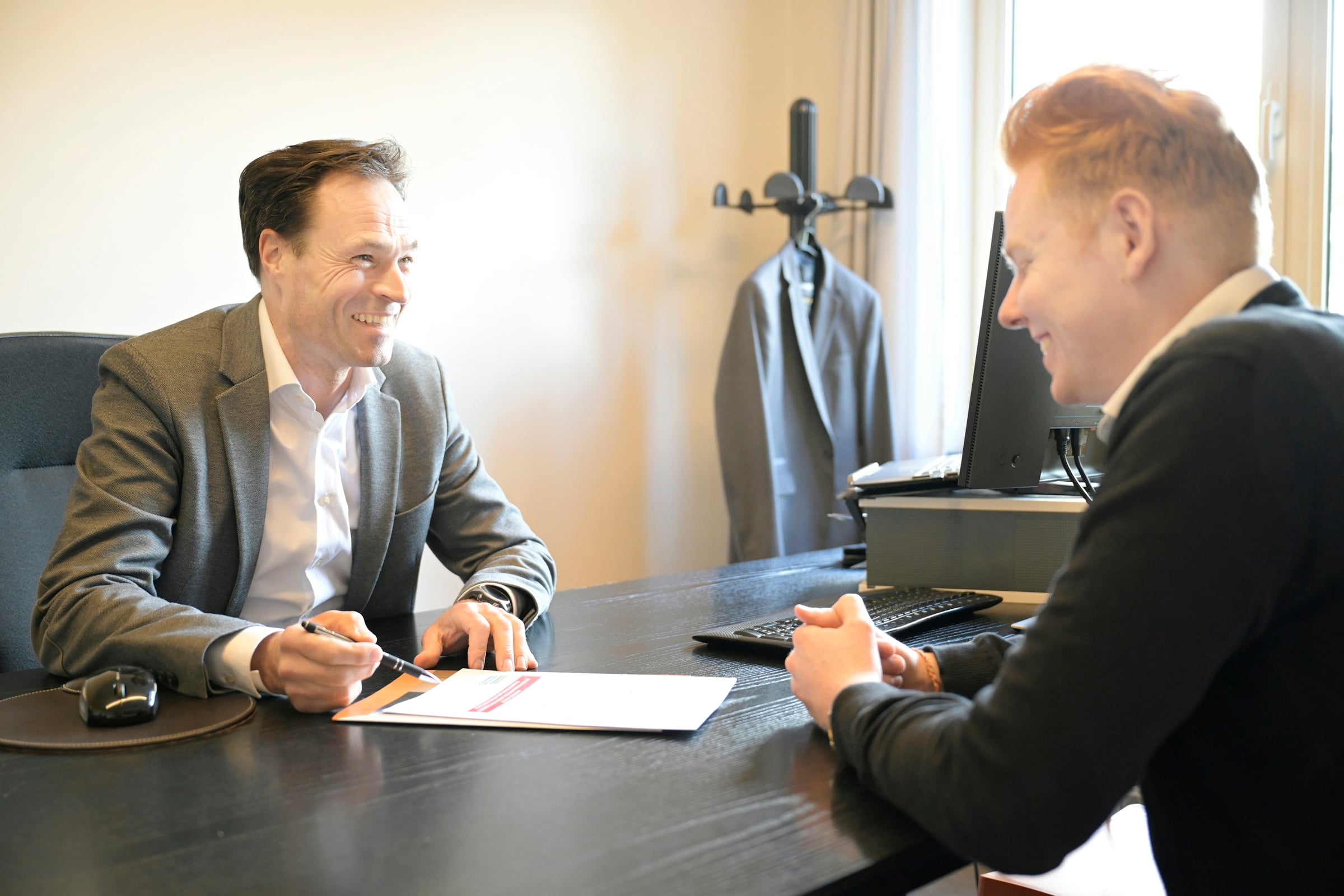 Two people seated at an office desk discussing a set of printed documents